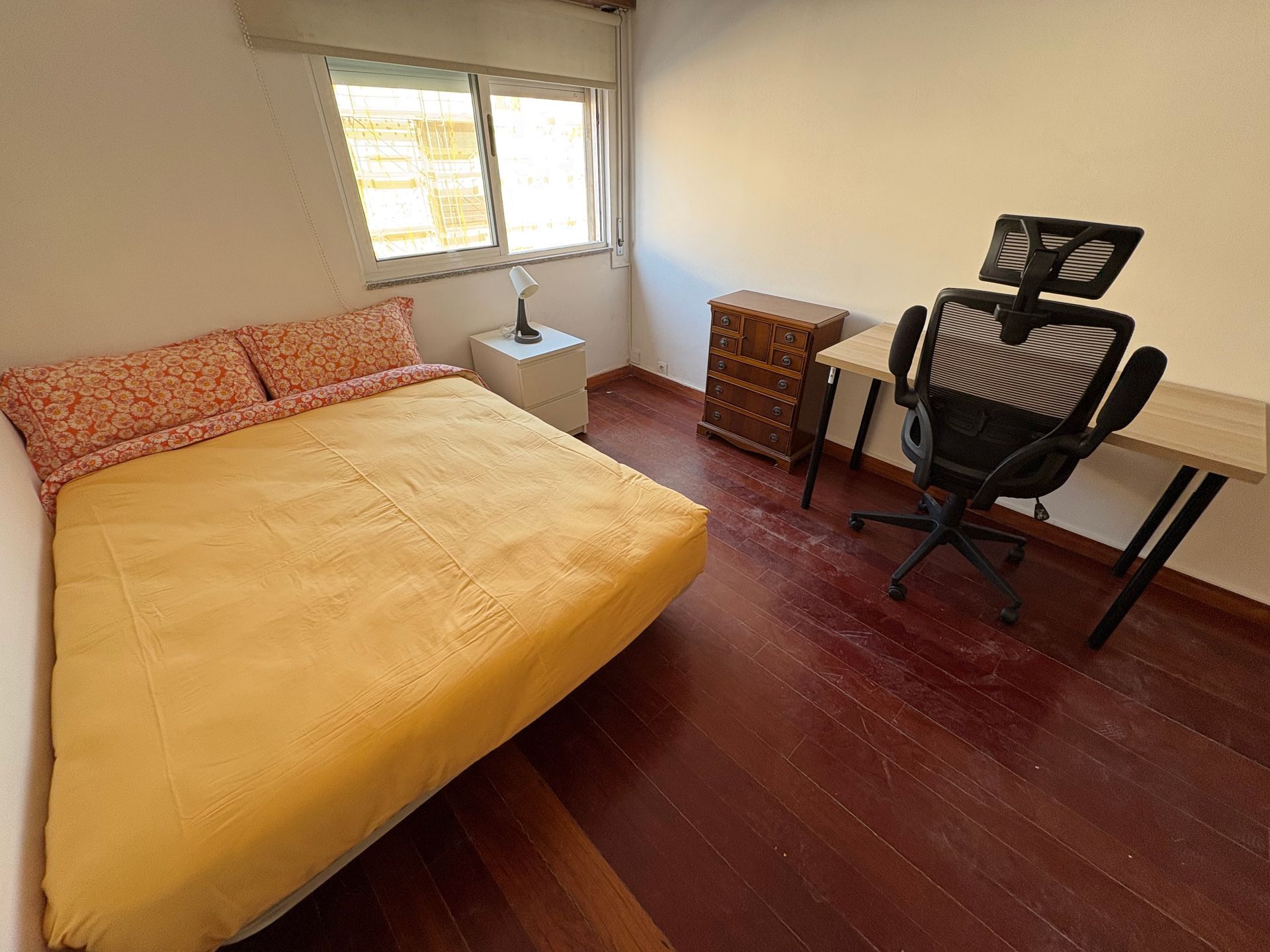 Bedroom with yellow bed, window, chair, and music stand on dark wooden floor.