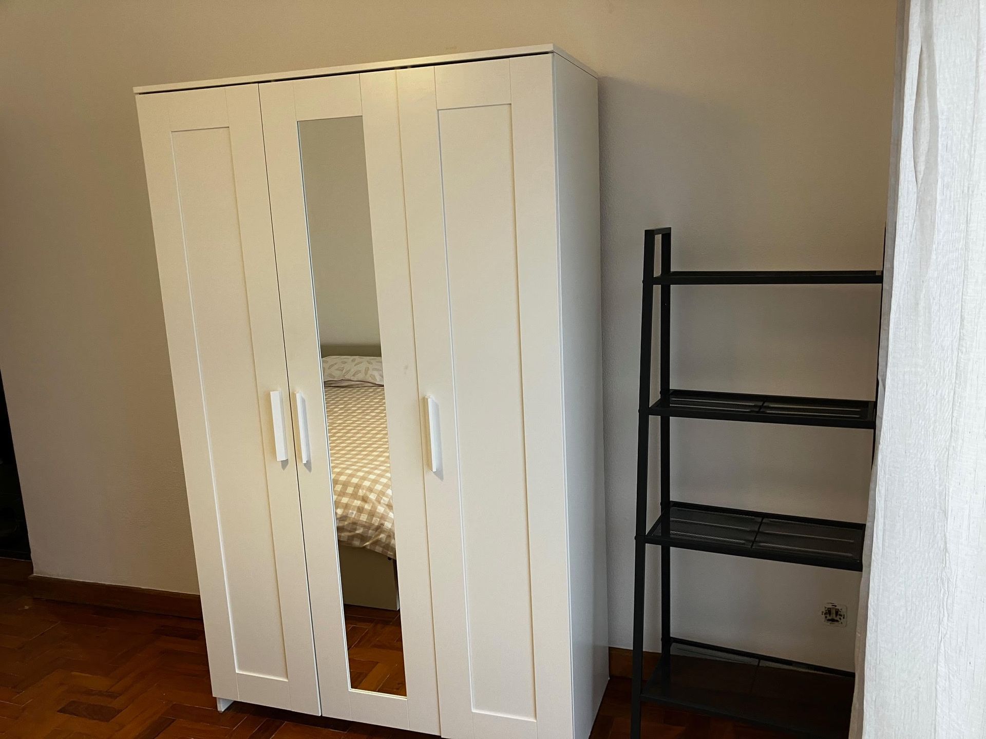 A bedroom with a white wardrobe and a black shelf