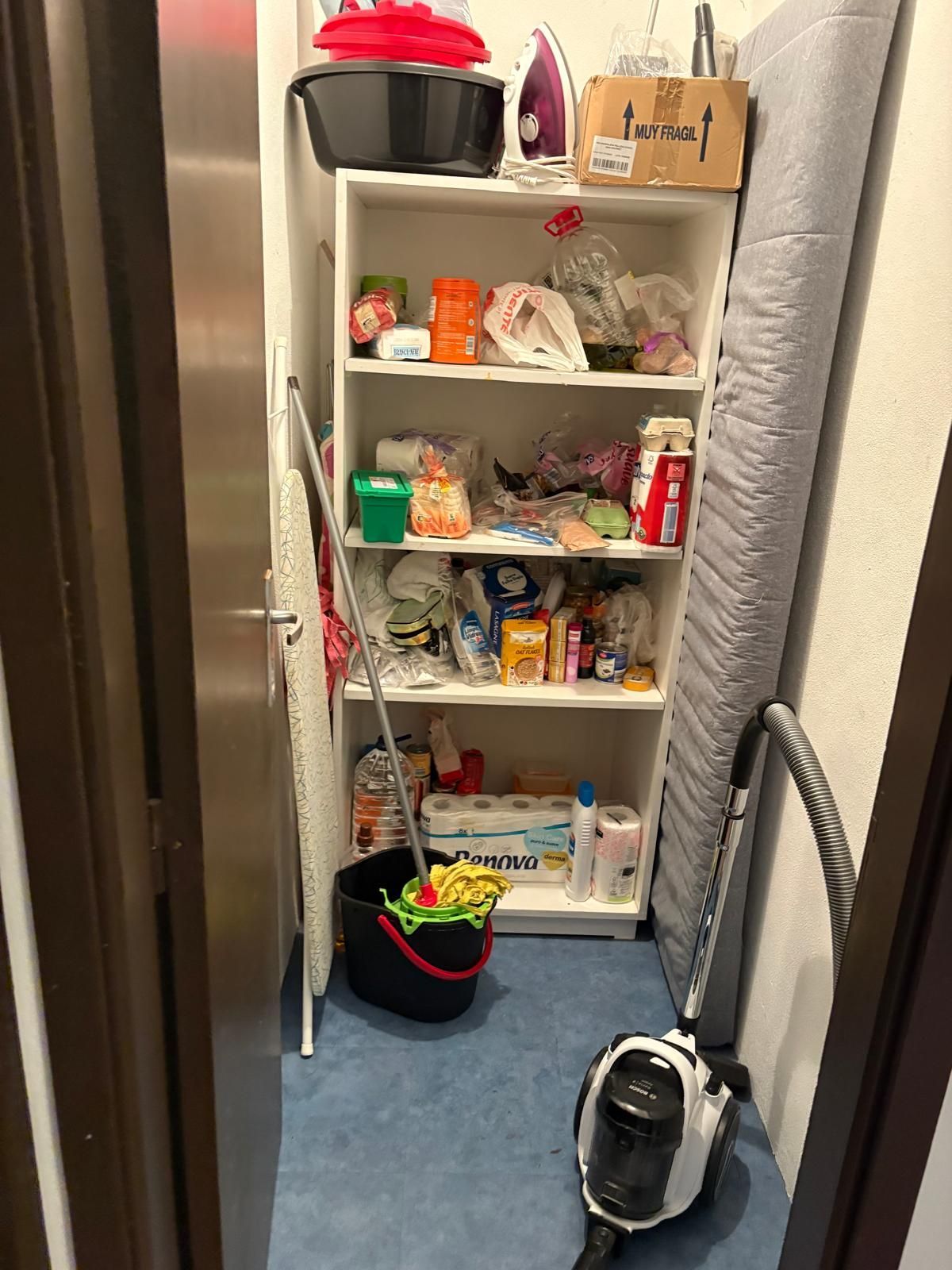 A pantry with a vacuum cleaner and a box that says ' tesco ' on it