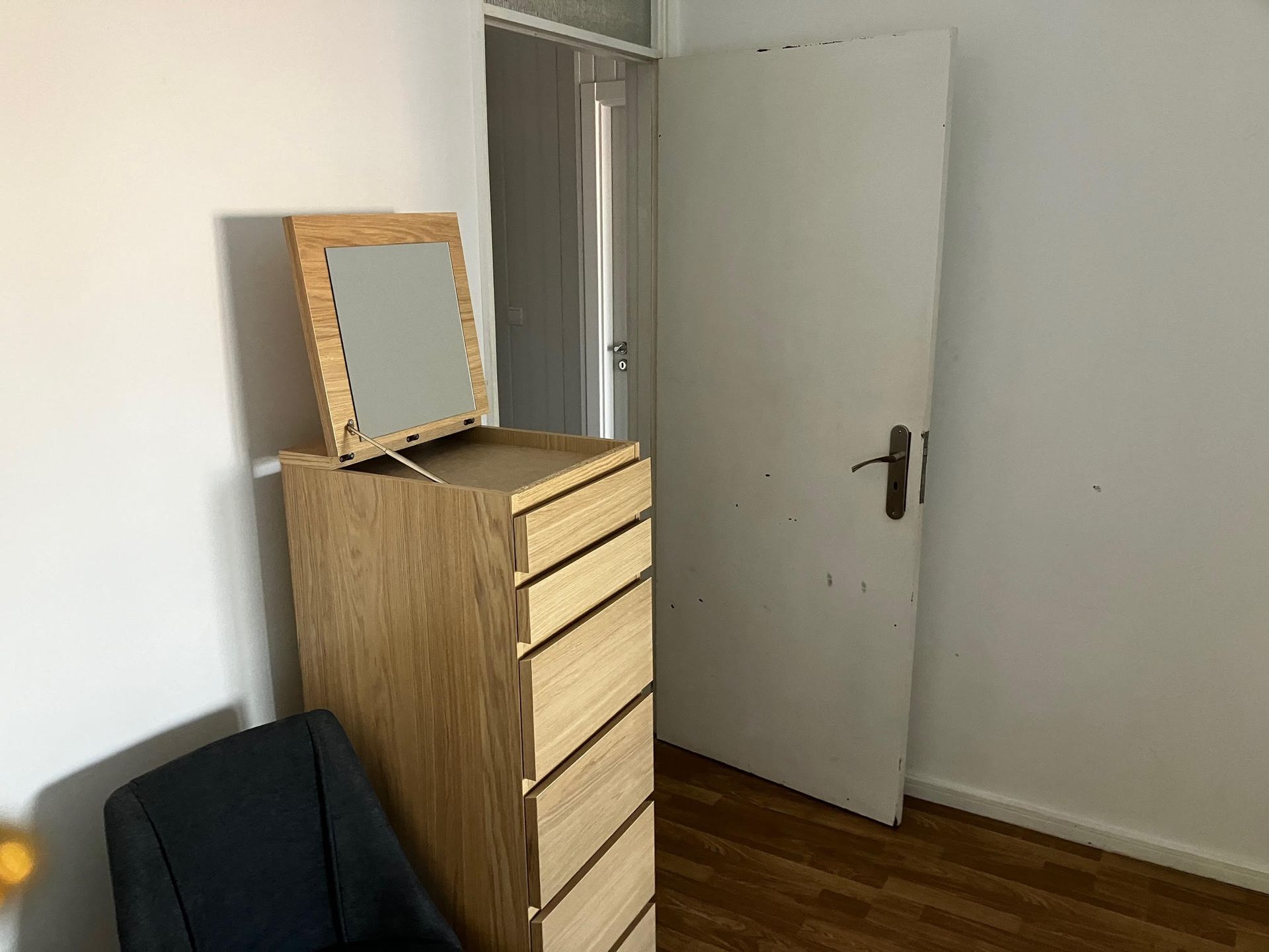 A room with a chair a dresser and a mirror