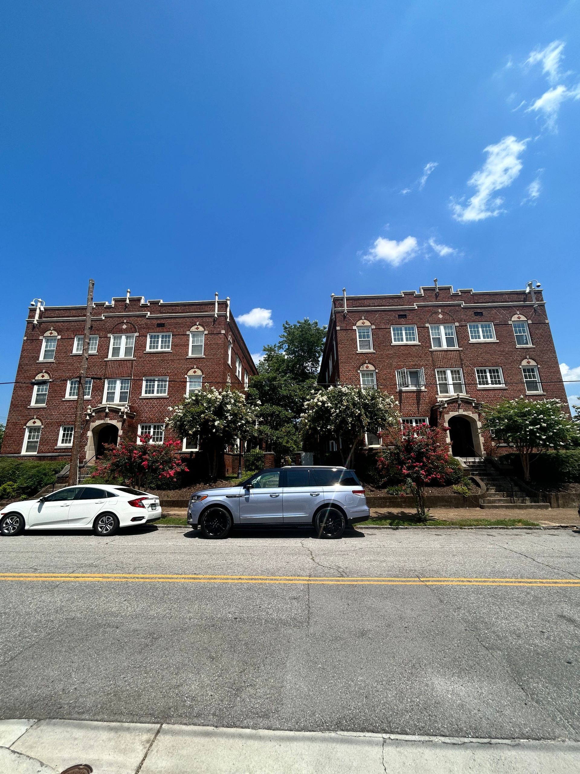 Red brick apartment building with rectangular windows against a blue sky with clouds.