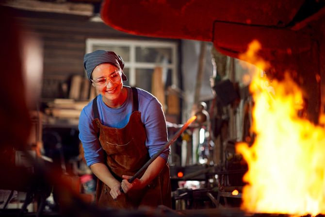 A woman is working on a piece of metal in a forge.