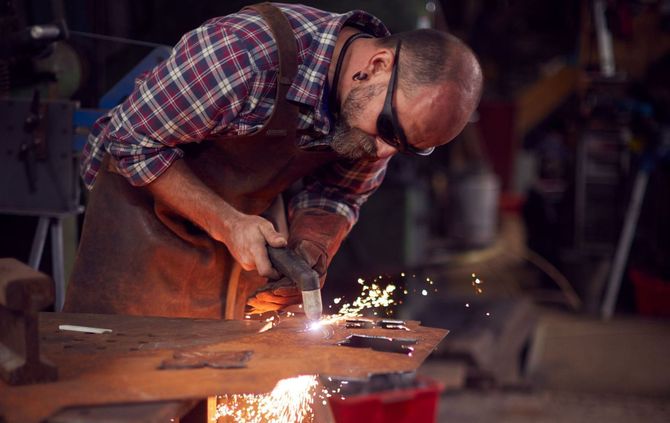 A man is welding a piece of metal on an anvil in a workshop.