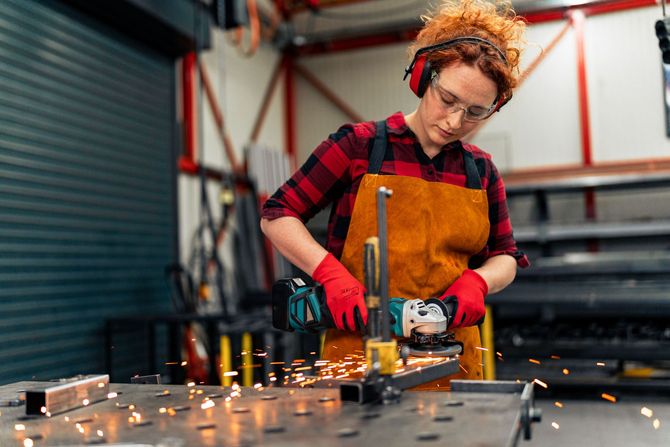 A woman is grinding a piece of metal in a factory.