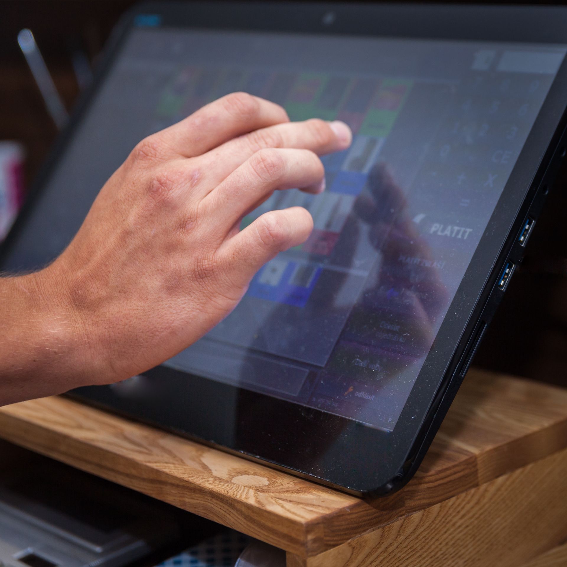 Hand interacting with a touch screen, likely a point-of-sale system, on a wooden stand. Hand interacting with a touch screen, likely a point-of-sale system, on a wooden stand.