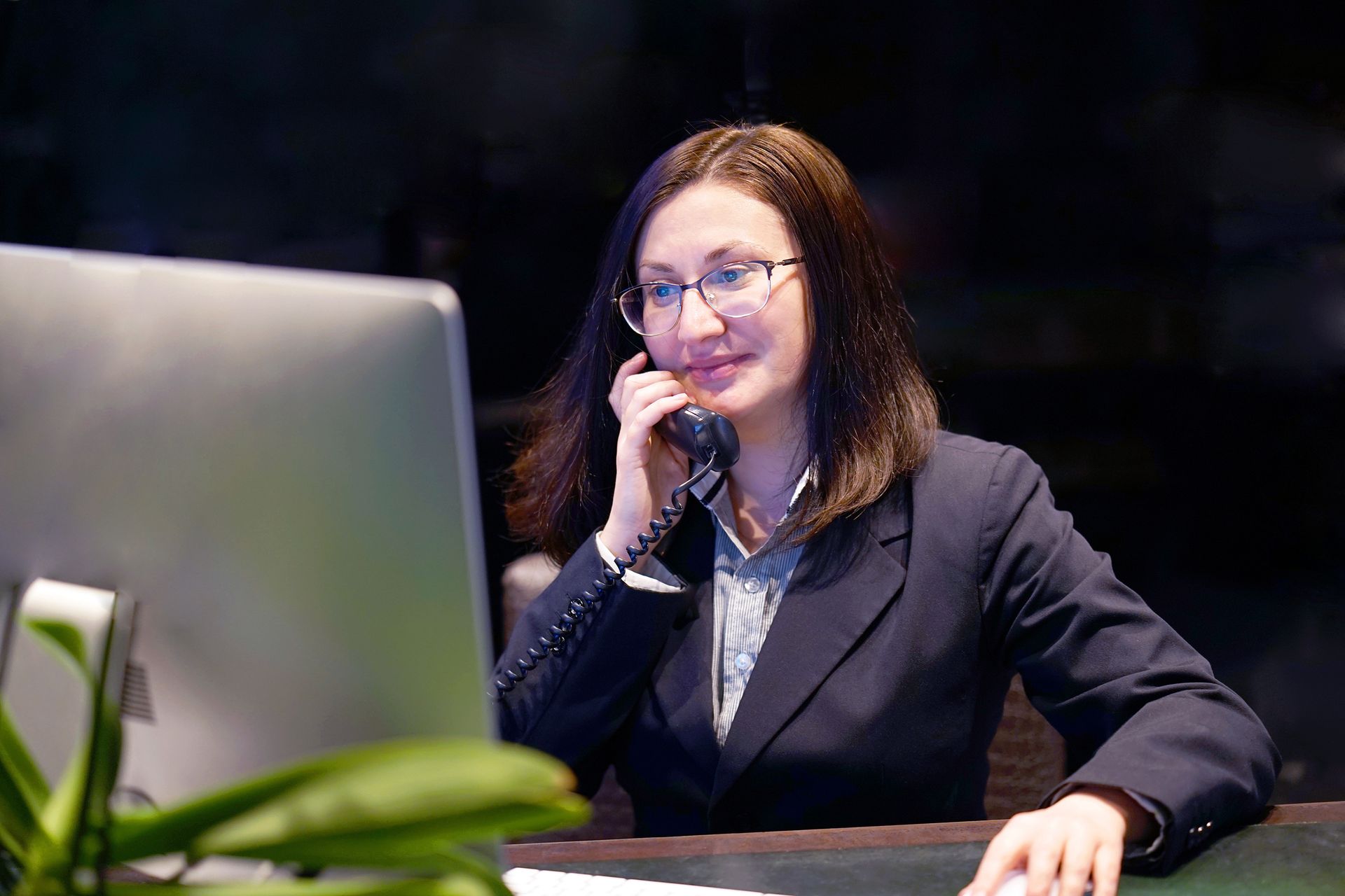 Woman in a dark suit wearing glasses, talking on the phone.
