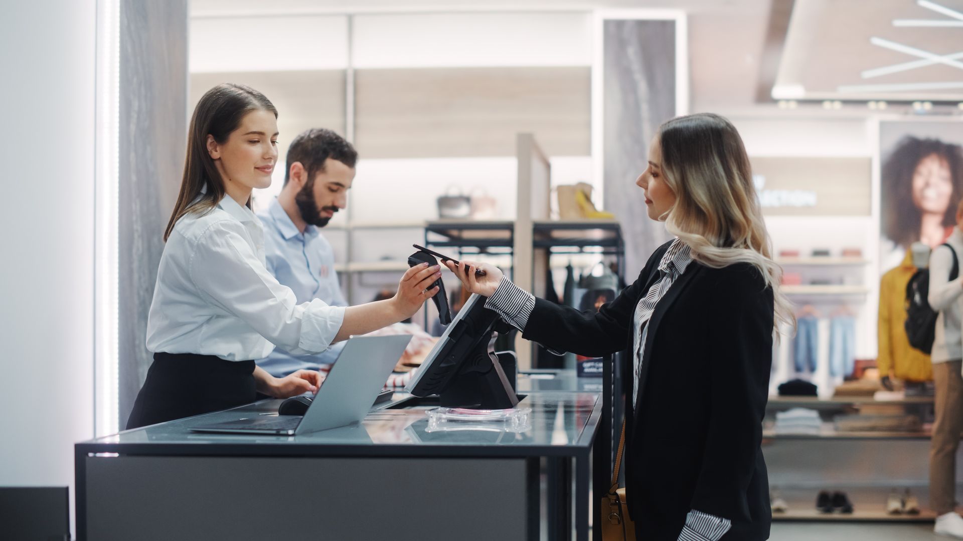 Woman paying at a store counter. A cashier hands over a shopping bag. Another person works at the register. Woman paying at a store counter. A cashier hands over a shopping bag. Another person works at the register.