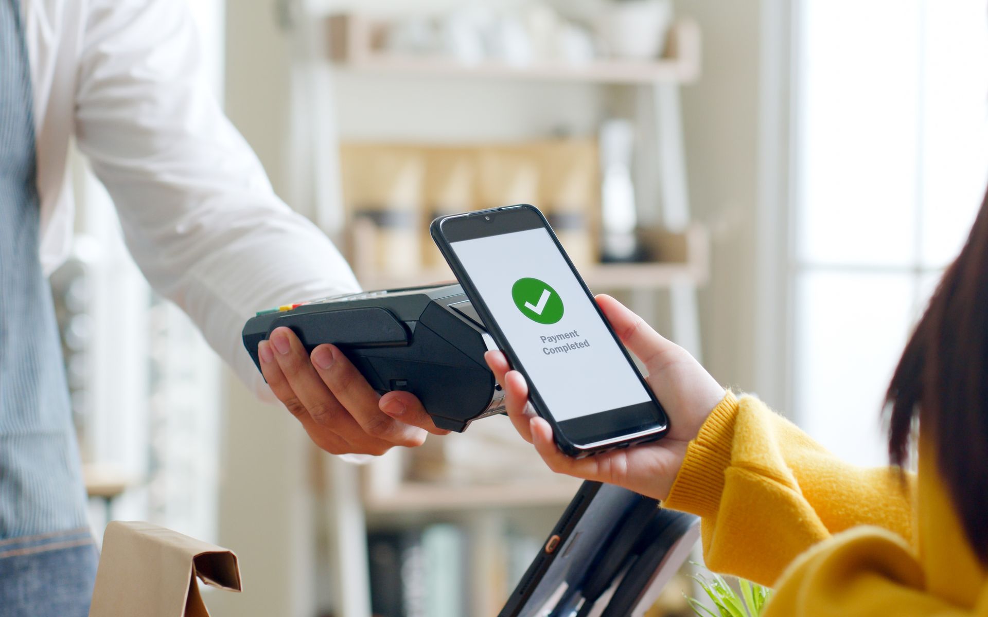 Person uses phone to make a contactless payment at a shop. Person uses phone to make a contactless payment at a shop.