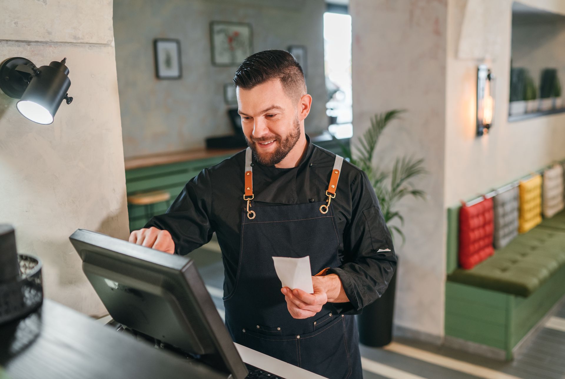 Man in black apron at a cash register, smiling. Man in black apron at a cash register, smiling.