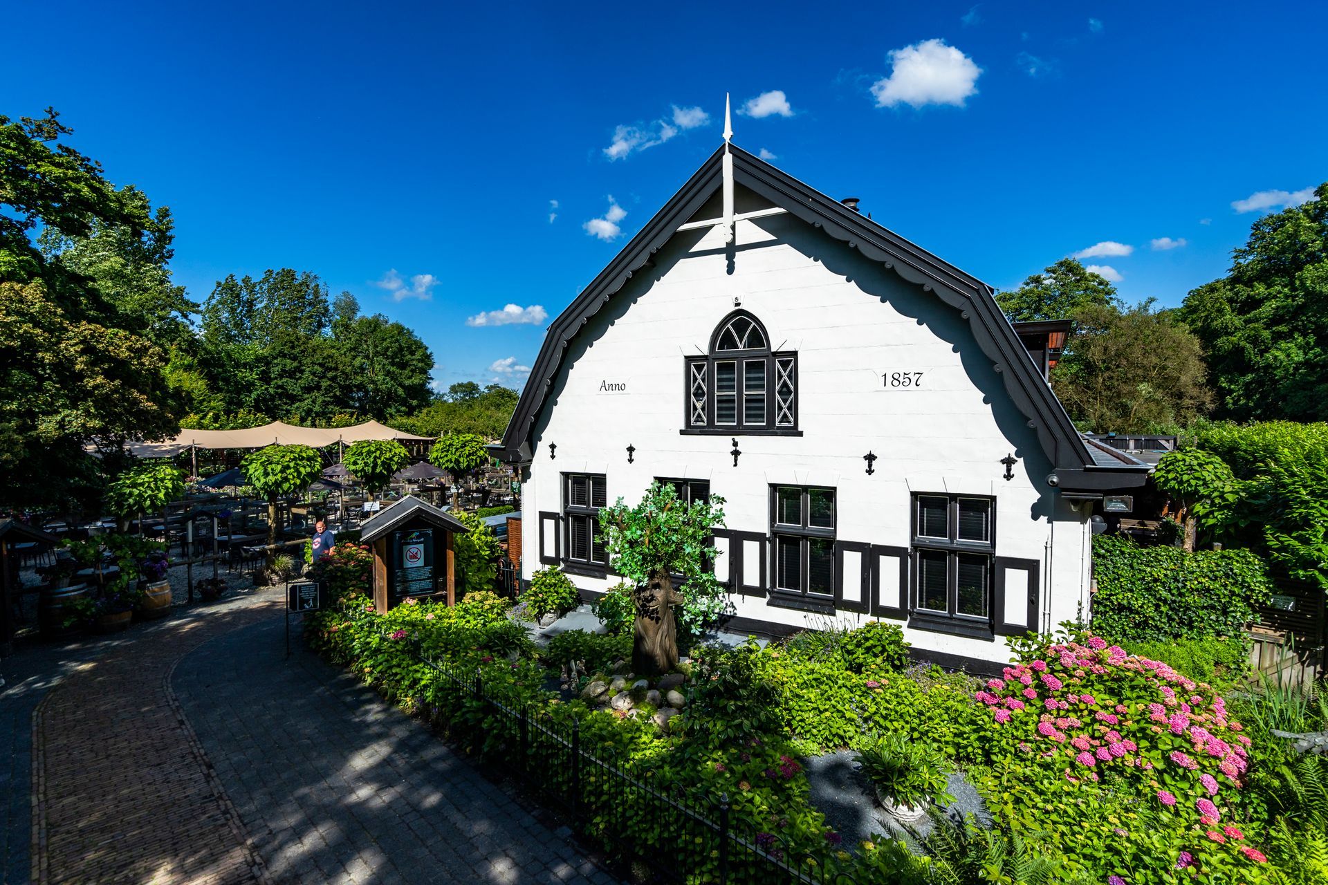 Witte boerderij met zwarte accenten, omgeven door groen onder een helderblauwe hemel.