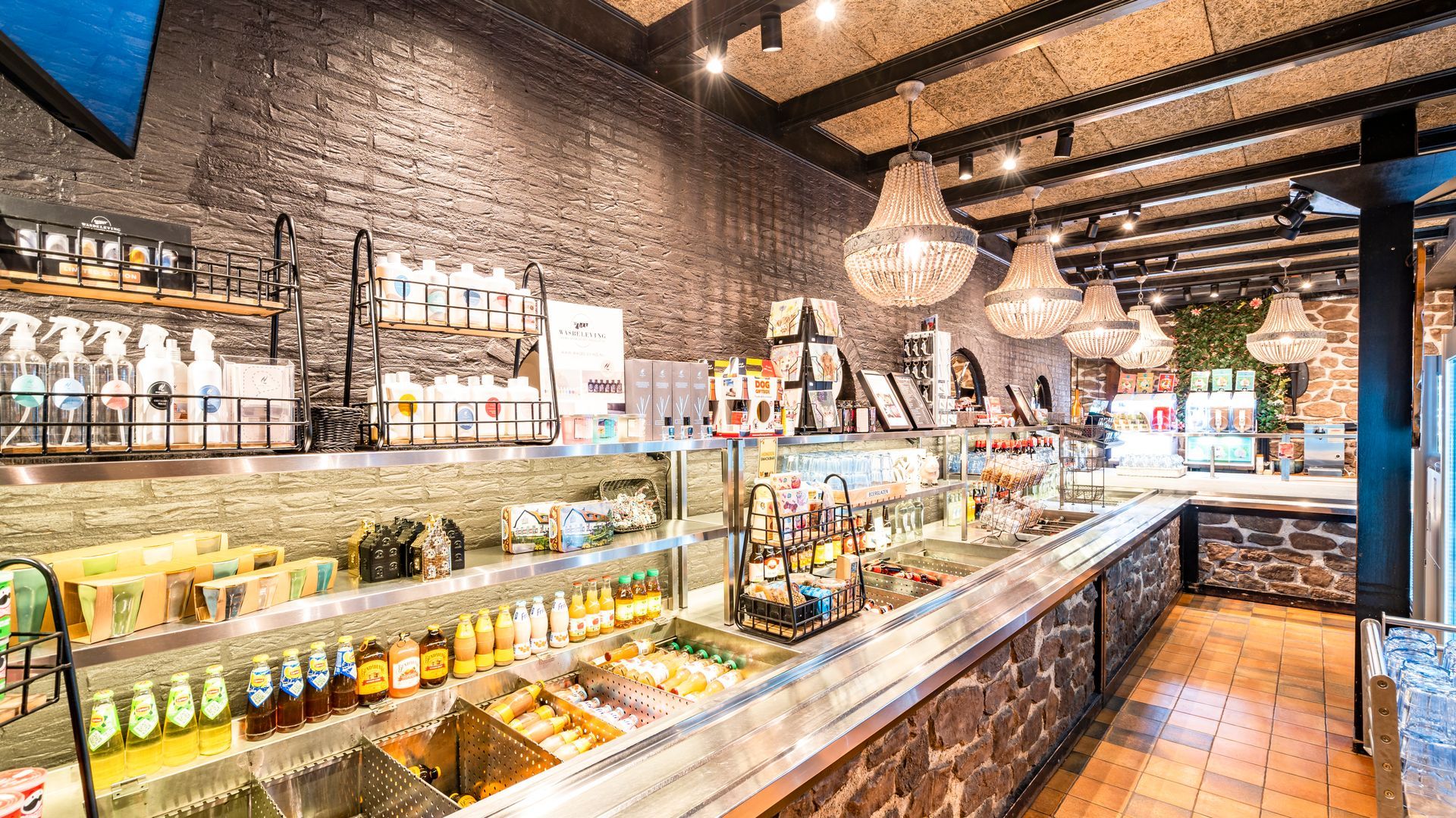 Binnen in een goed verlicht café met een toonbank waarop eten en drinken worden uitgestald; kroonluchters hangen aan het plafond.