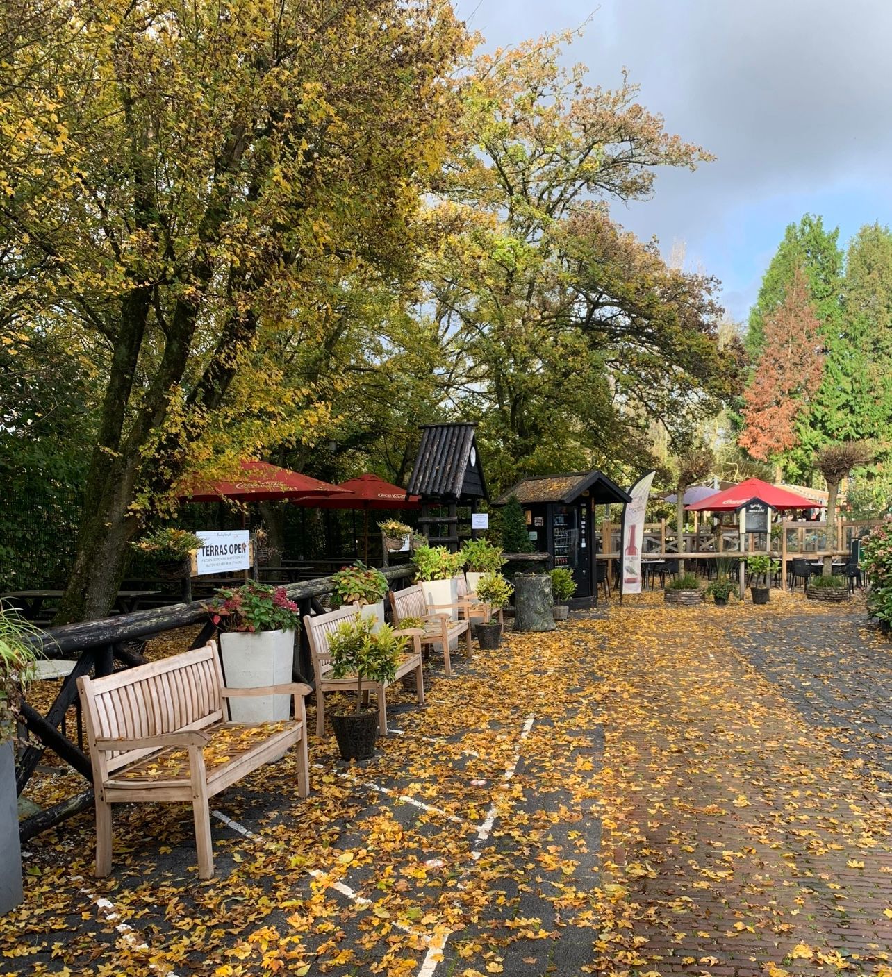 Het pad is omzoomd met bankjes, potplanten en overdekte zitjes onder herfstbomen.