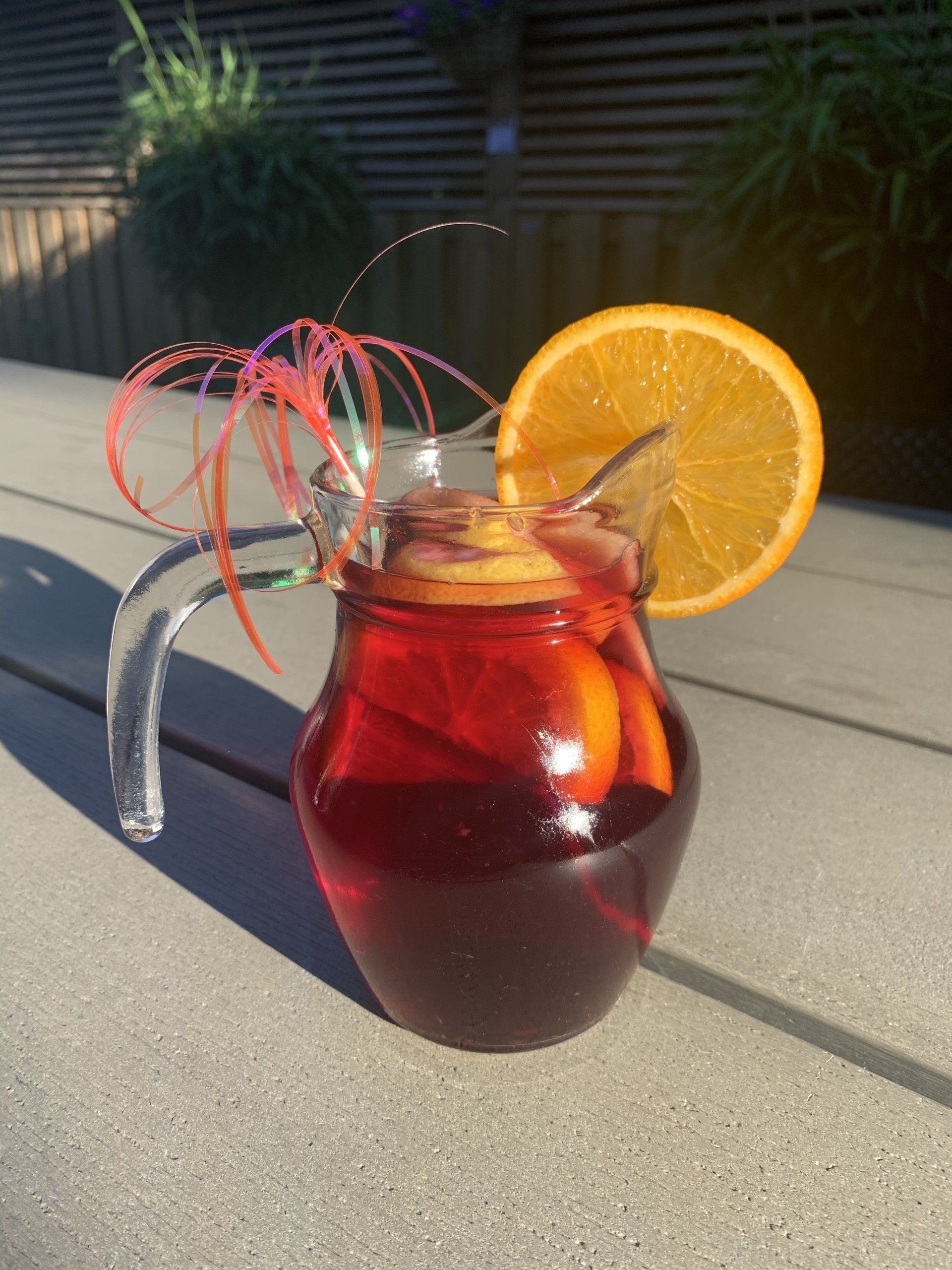 Sangria in een glazen karaf met een schijfje sinaasappel, rode vloeistof, buiten op een grijze ondergrond.
