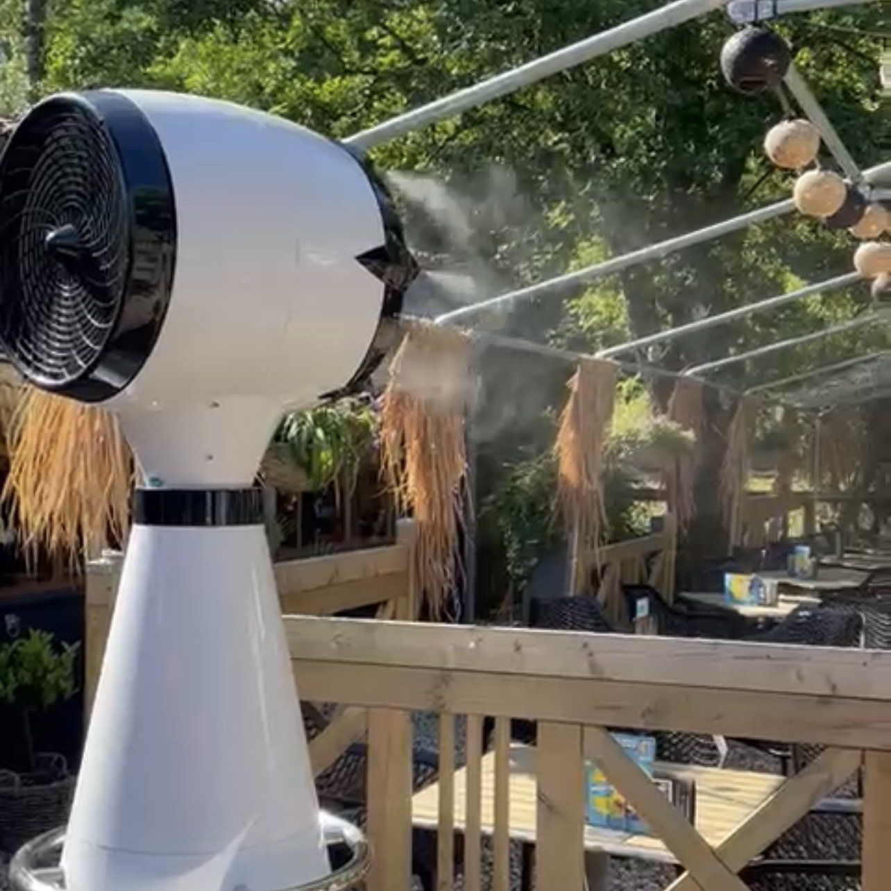 Witte vernevelingsventilator voor buiten op een houten terras in een schaduwrijk buiteneetgedeelte.