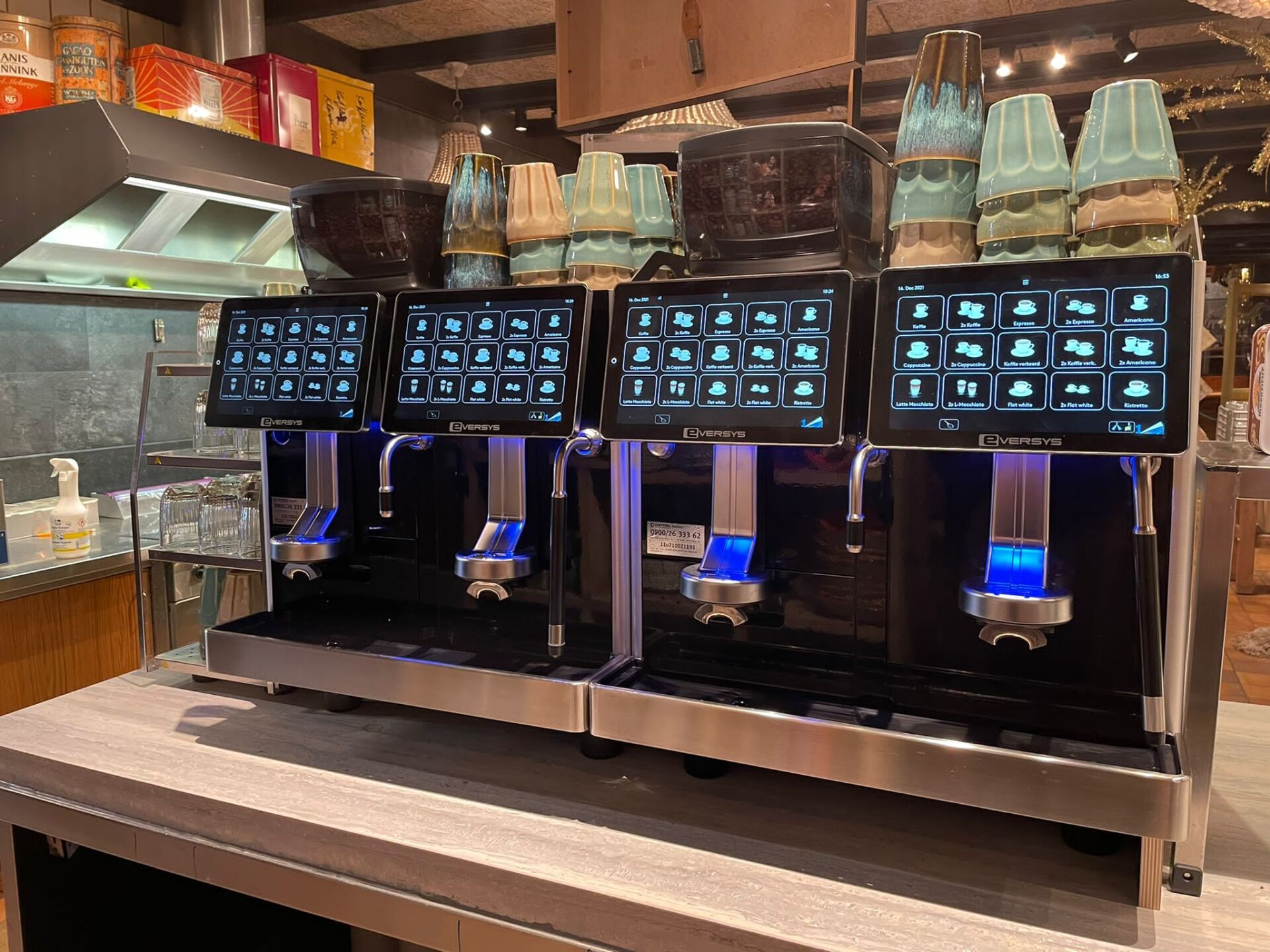 Vier drankautomaten met touchscreen, blauwe verlichting en diverse drankopties.