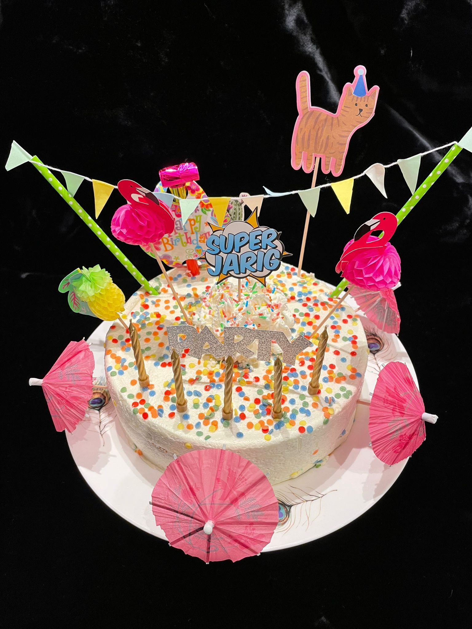 Witte cake met hagelslag, versieringen en kaarsjes, geserveerd op een wit bord.