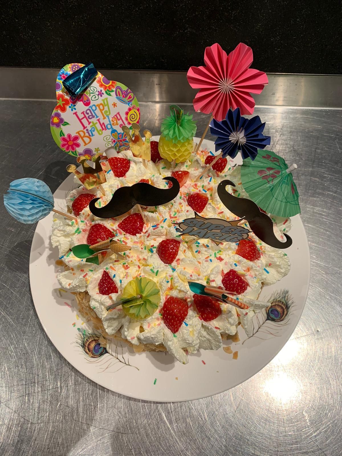 Taart versierd met slagroom, aardbeien, snorretjes en kleurrijke decoraties.