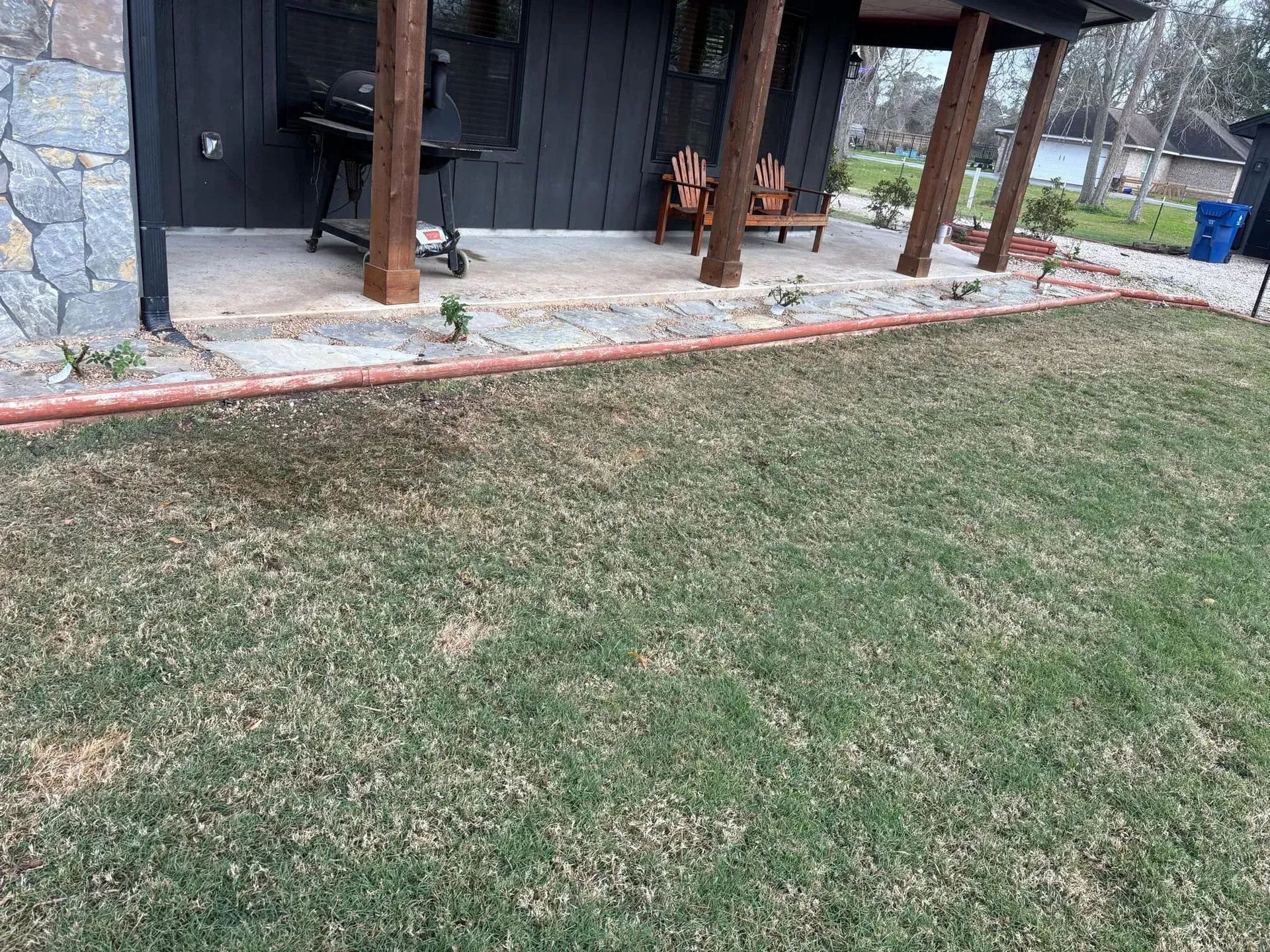 A house exterior with a concrete patio and a small lawn. The house has dark siding and stone accents.