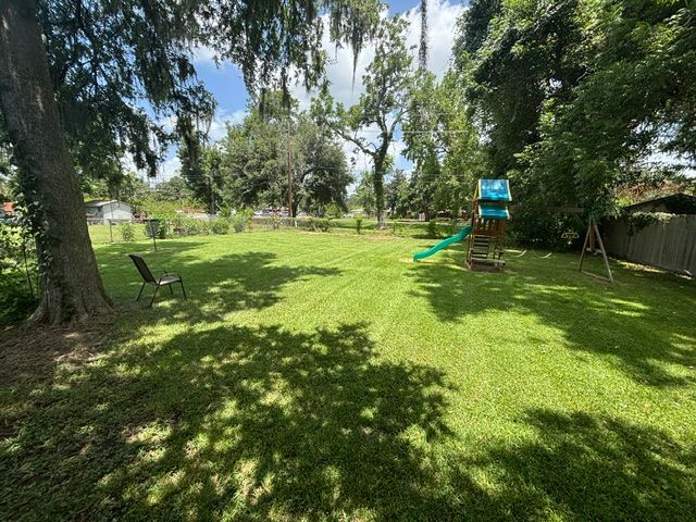 Grassy backyard with a play set. A tree casts a shadow over a chair and part of the lawn under a partly cloudy sky.