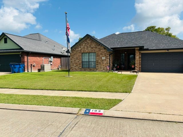 A Texas flag flies on a pole in front. Another house is on the left.