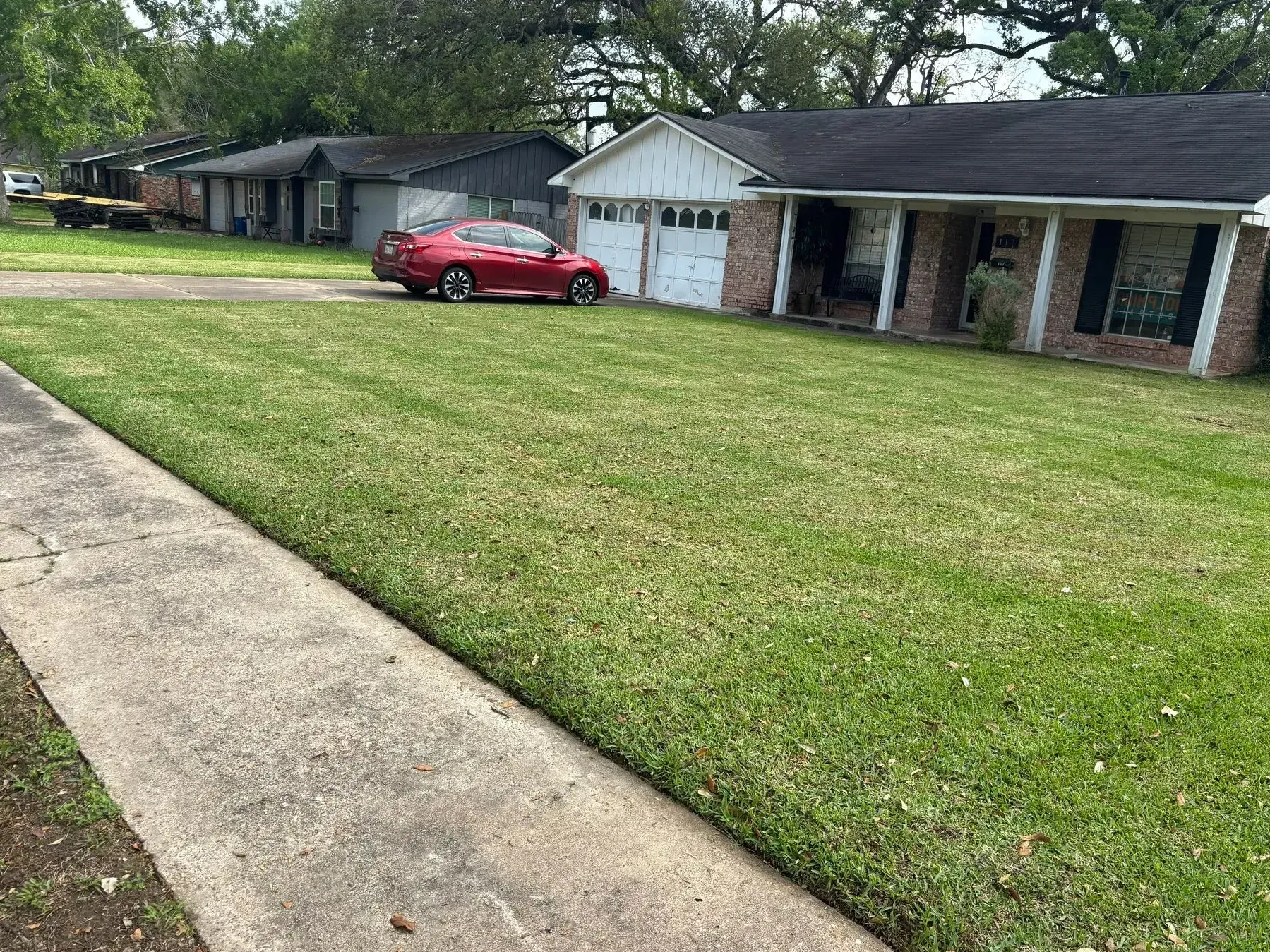 A well-maintained green lawn in front of a row of houses. A red car is parked near the center.