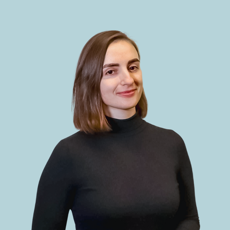 Woman with bob haircut wearing black turtleneck, smiling against a light blue background.