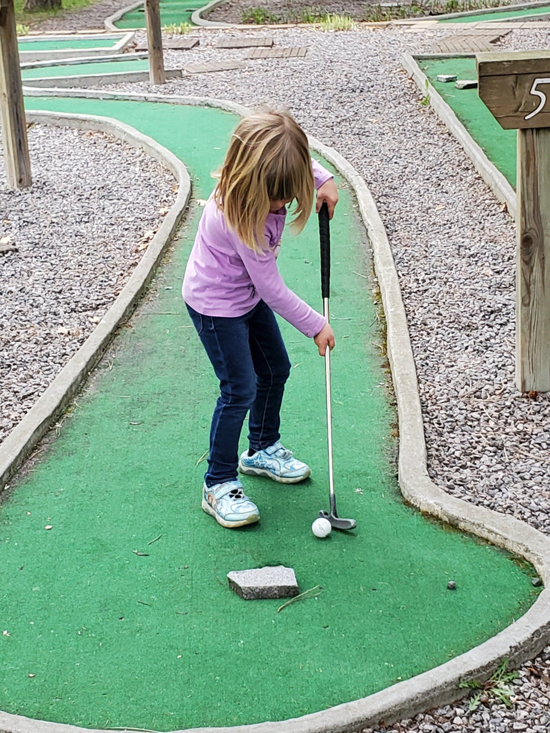 A little girl is playing mini golf on a green course.