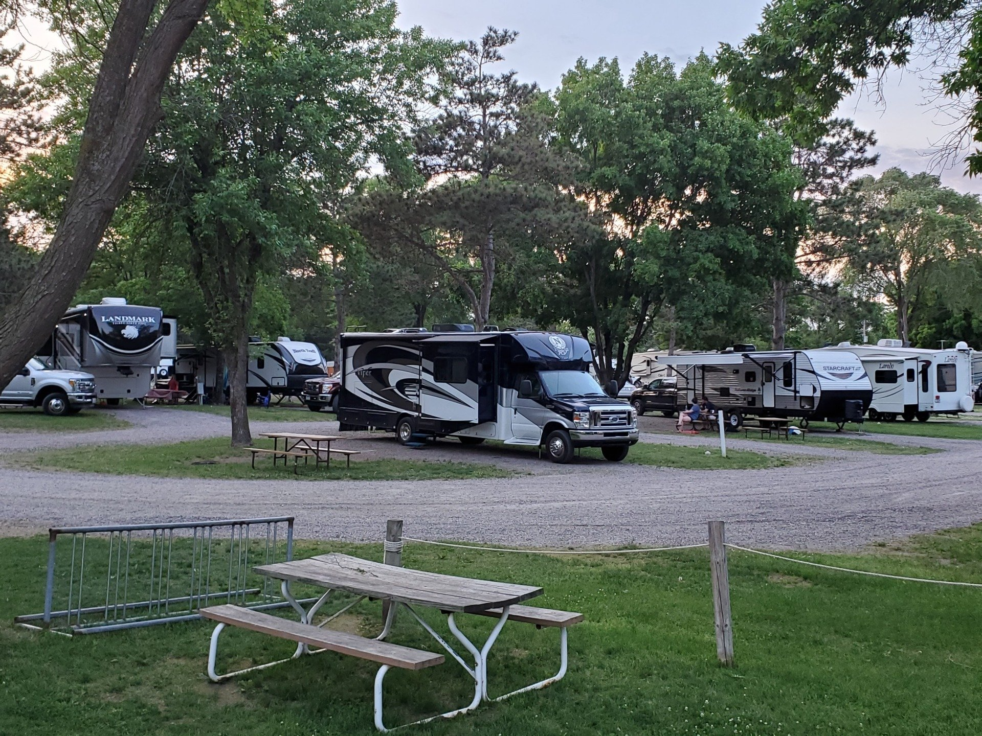 A group of rvs are parked in a lot with a picnic table.