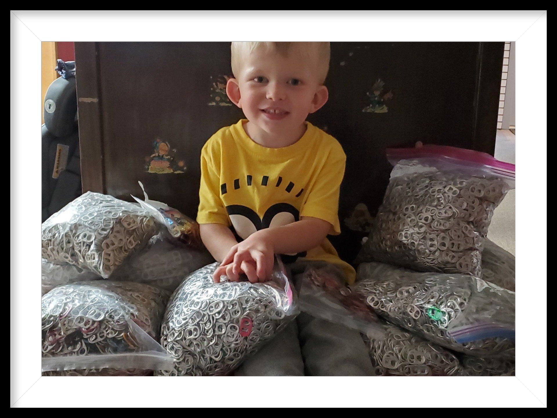 A young boy in a yellow shirt is sitting on a pile of bags of food.