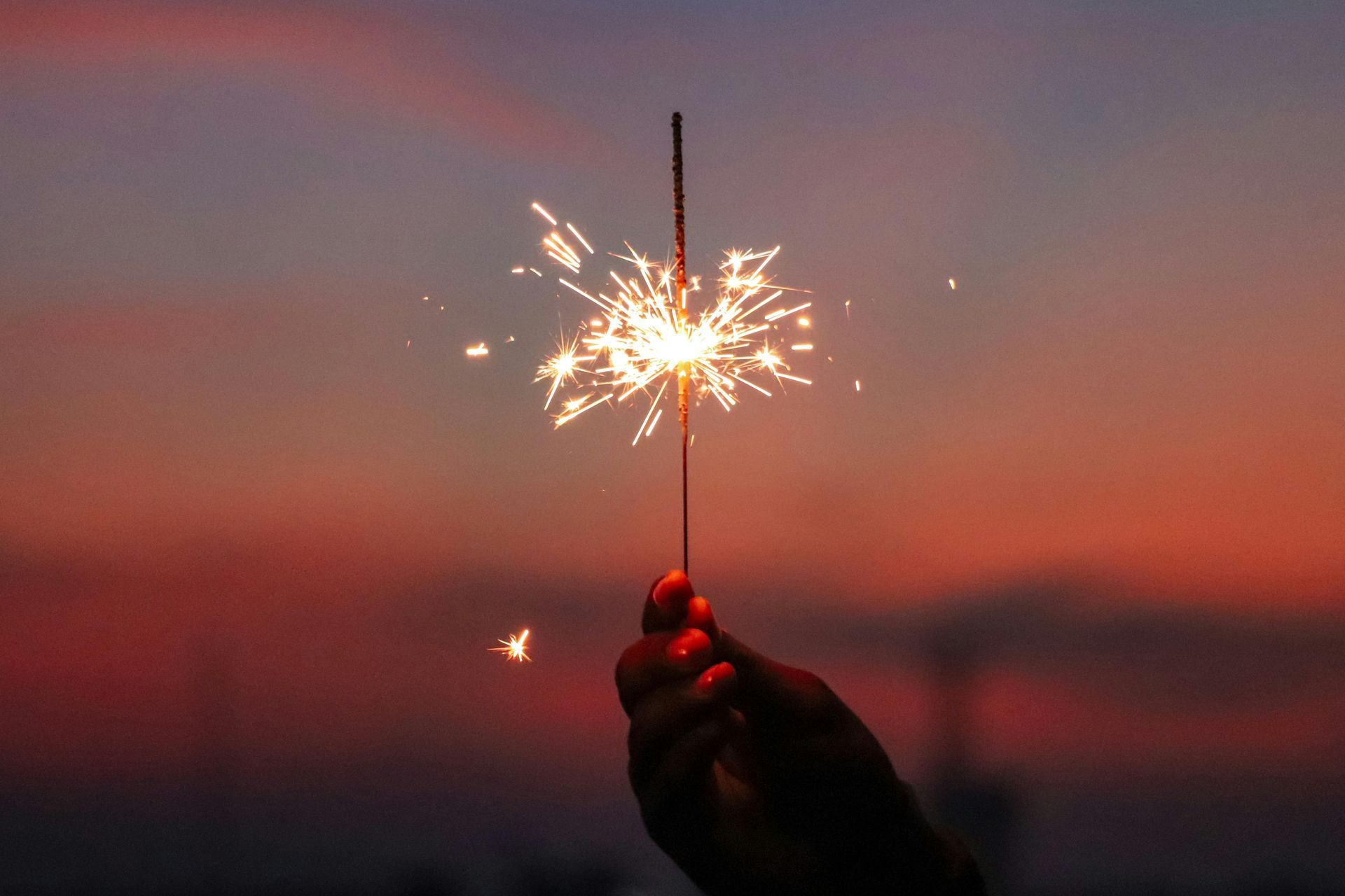 A person is holding a sparkler in their hand at sunset.