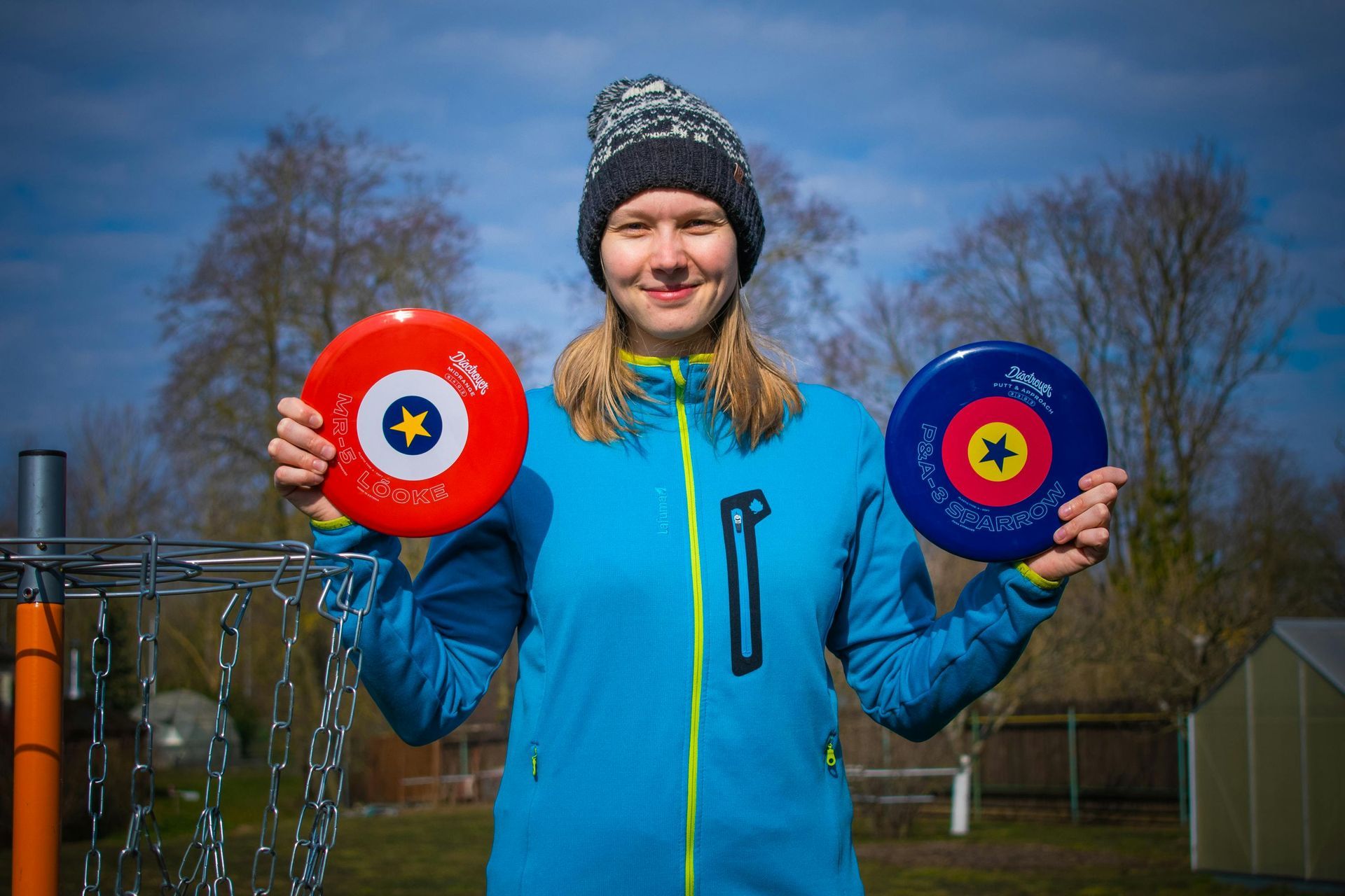 A woman in a blue jacket is holding two frisbees in her hands.