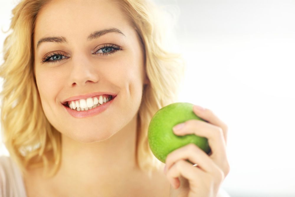 Young Woman With Denture Holding an Apple — The Denture Care Group Sunshine Coast in Caloundra, QLD