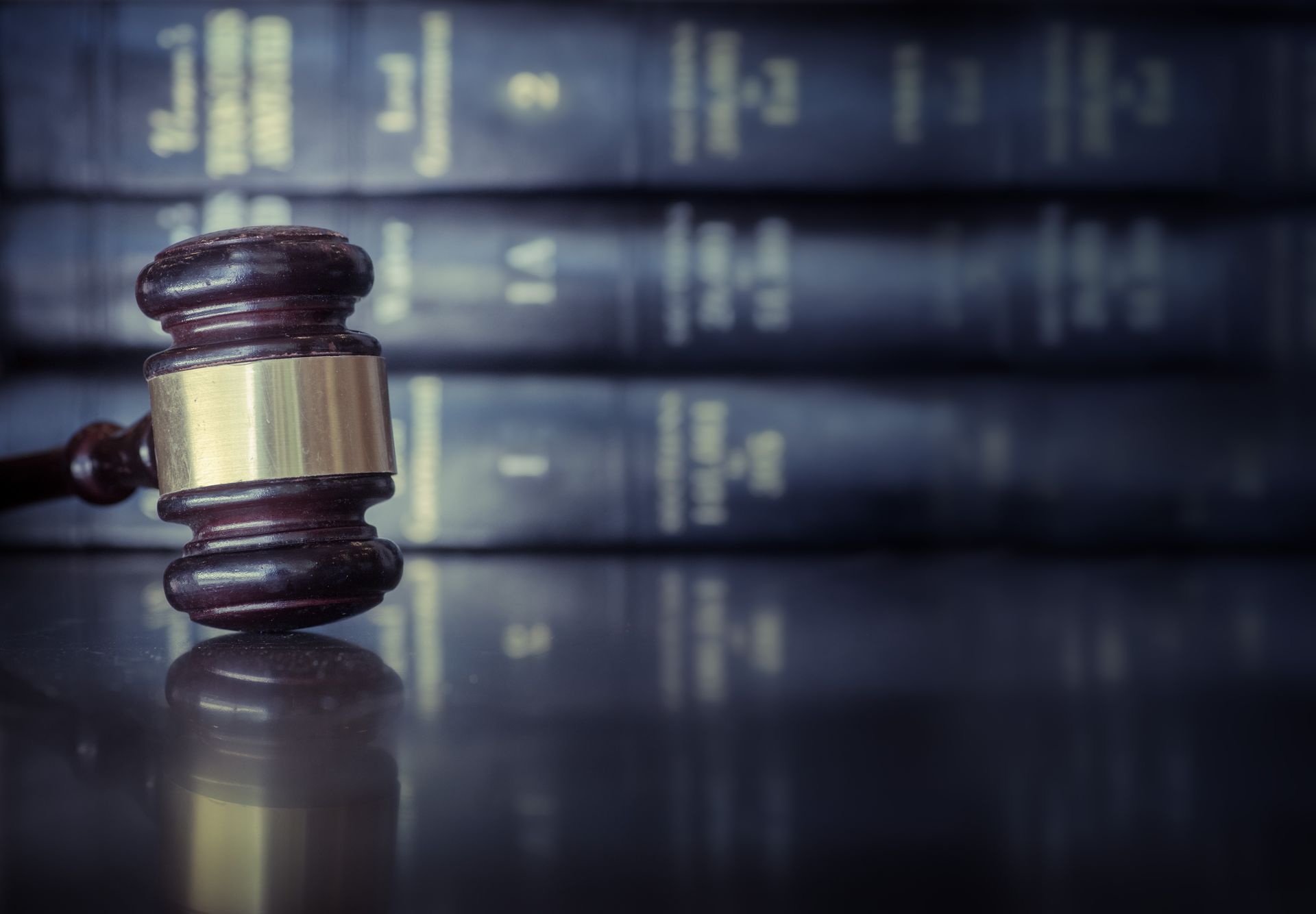 Wooden judge’s gavel resting on a reflective surface with blurred legal books in the background.