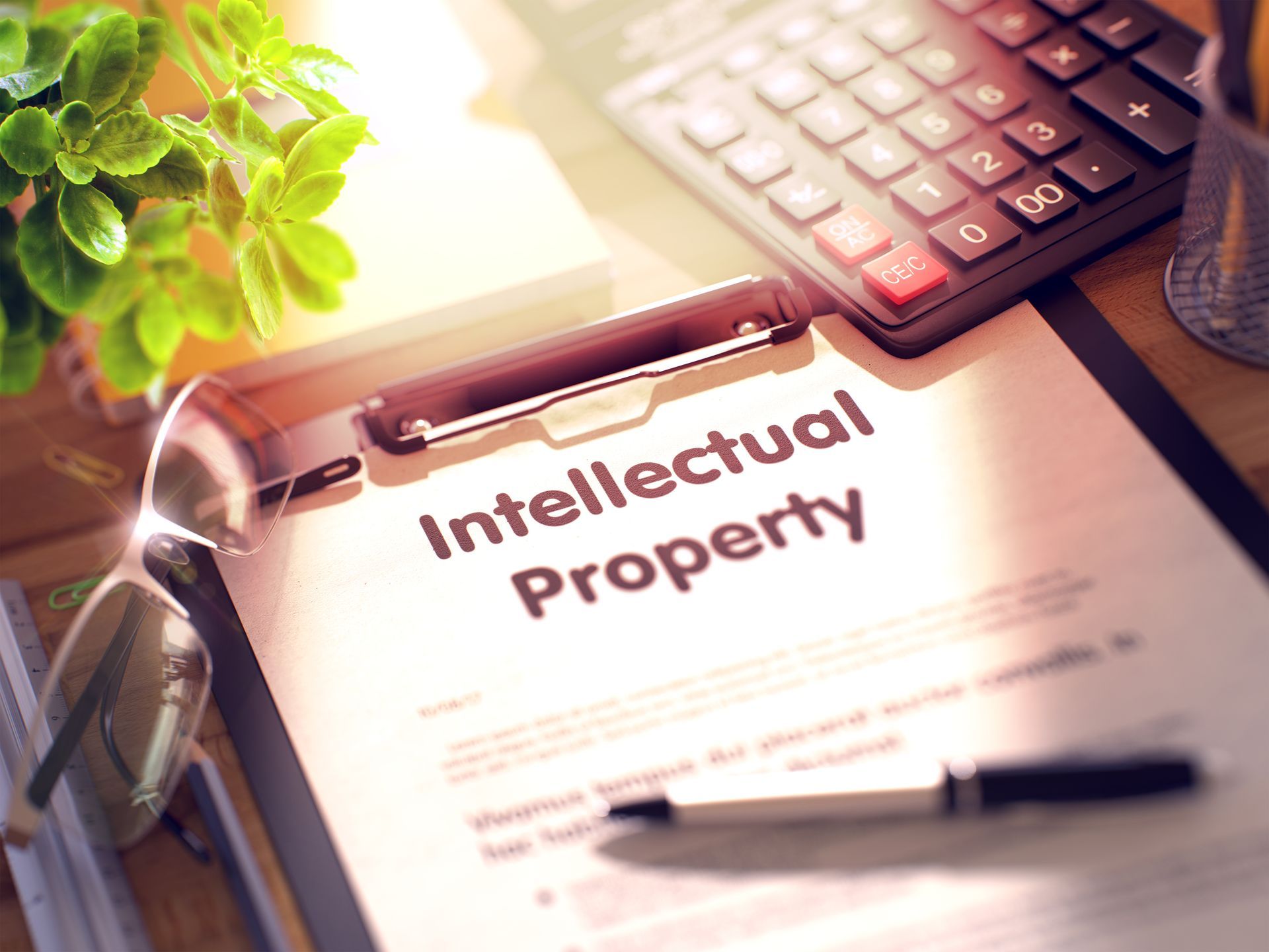 Clipboard labeled intellectual property beside a calculator and glasses on a sunlit desk. Clipboard labeled intellectual property beside a calculator and glasses on a sunlit desk.