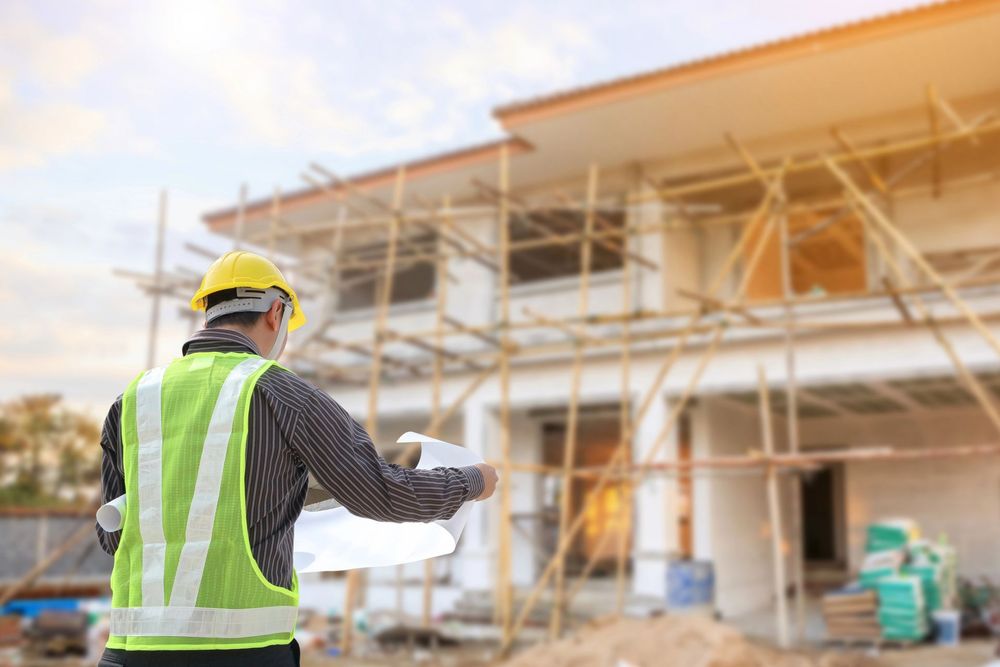 Operaio edile con elmetto giallo e giubbotto catarifrangente su un cantiere con impalcature.