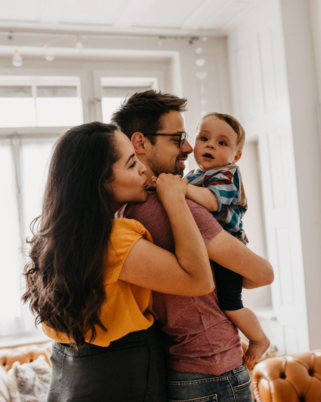 Family embracing a baby in a bright living room, with the mother and father holding the child close.