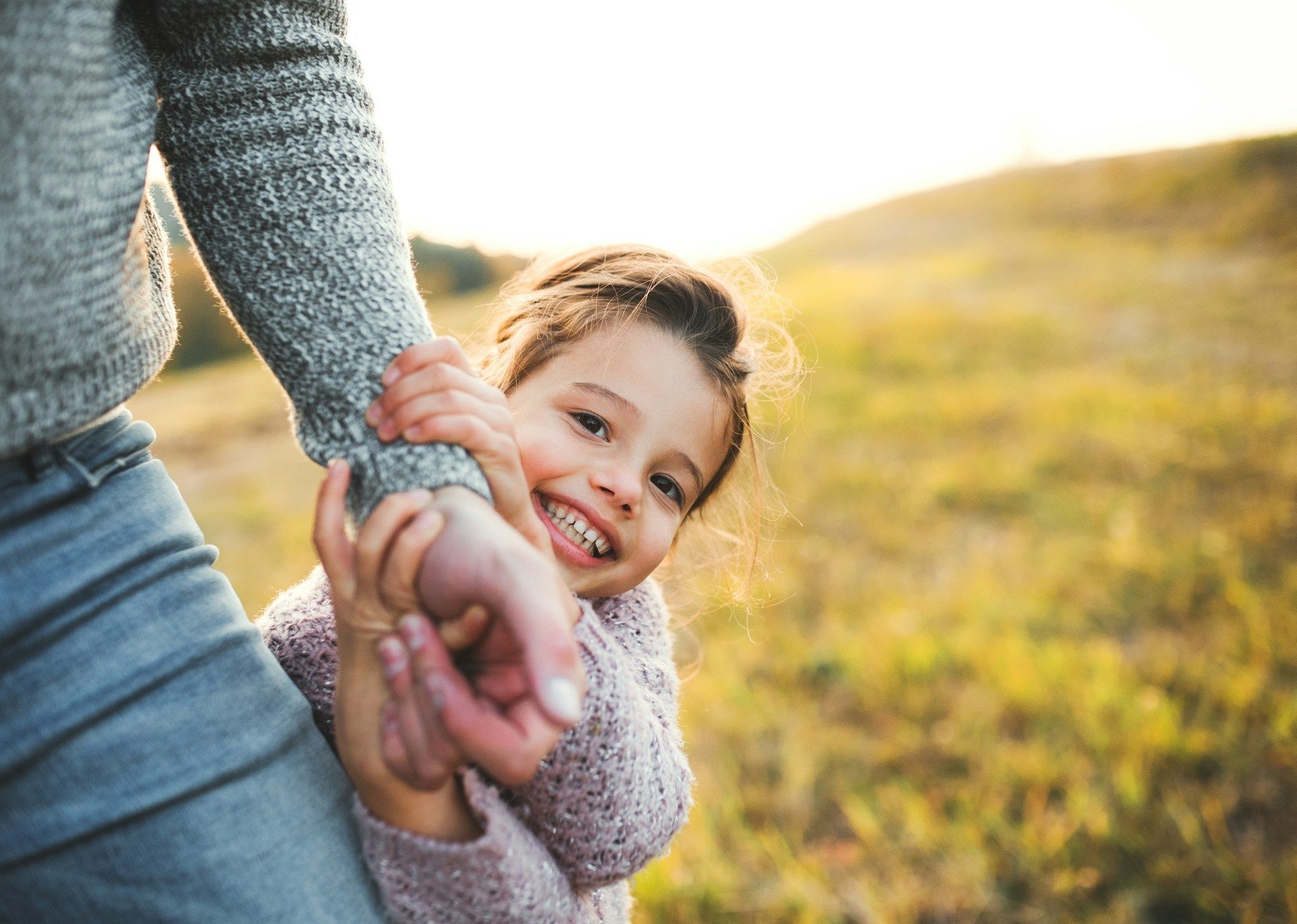 Adult and child holding hands in a sunlit field, smiling and walking together