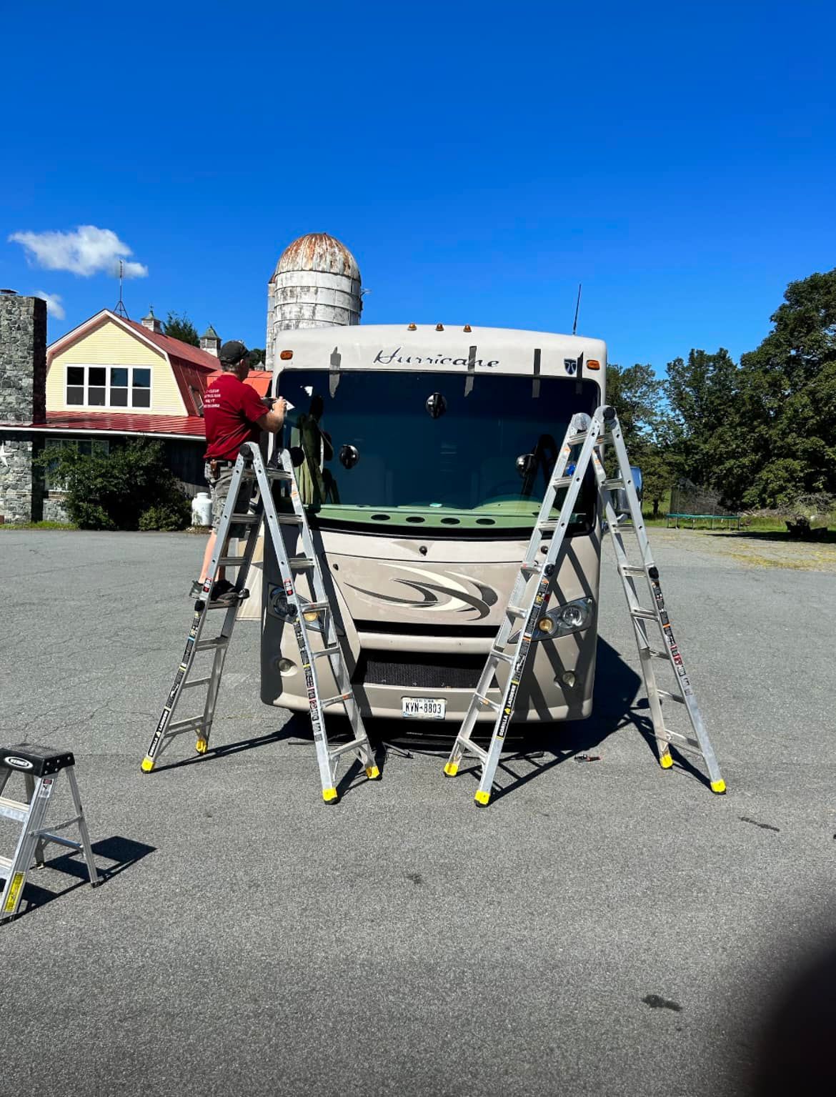 A man on a ladder is working on a rv in a parking lot.