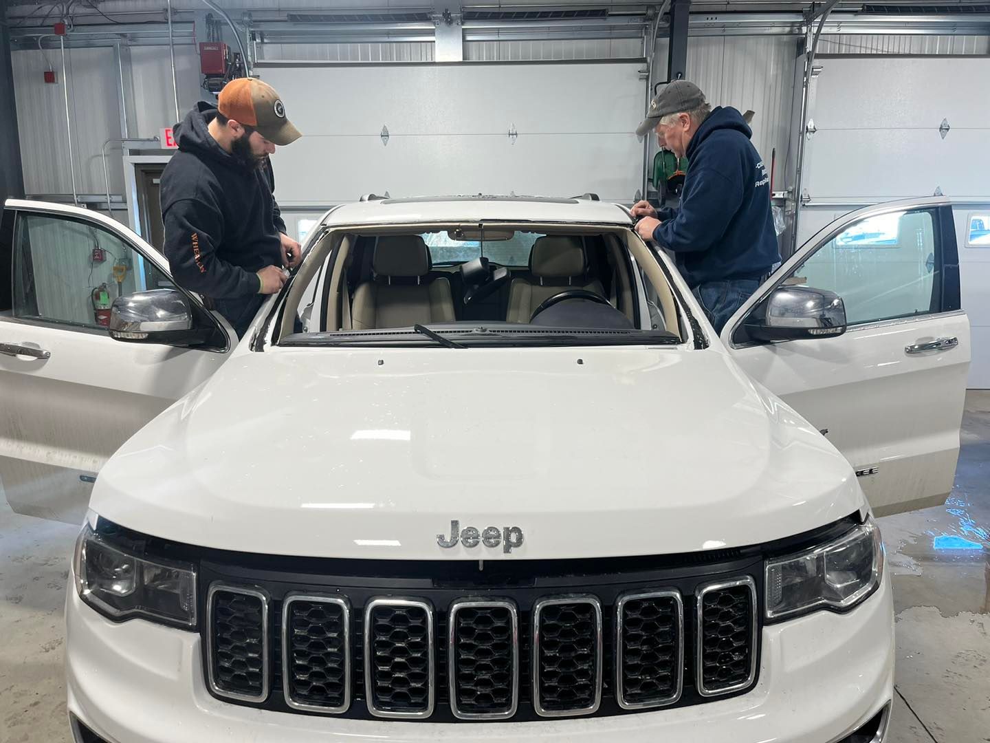 Two men are working on a white jeep in a garage.