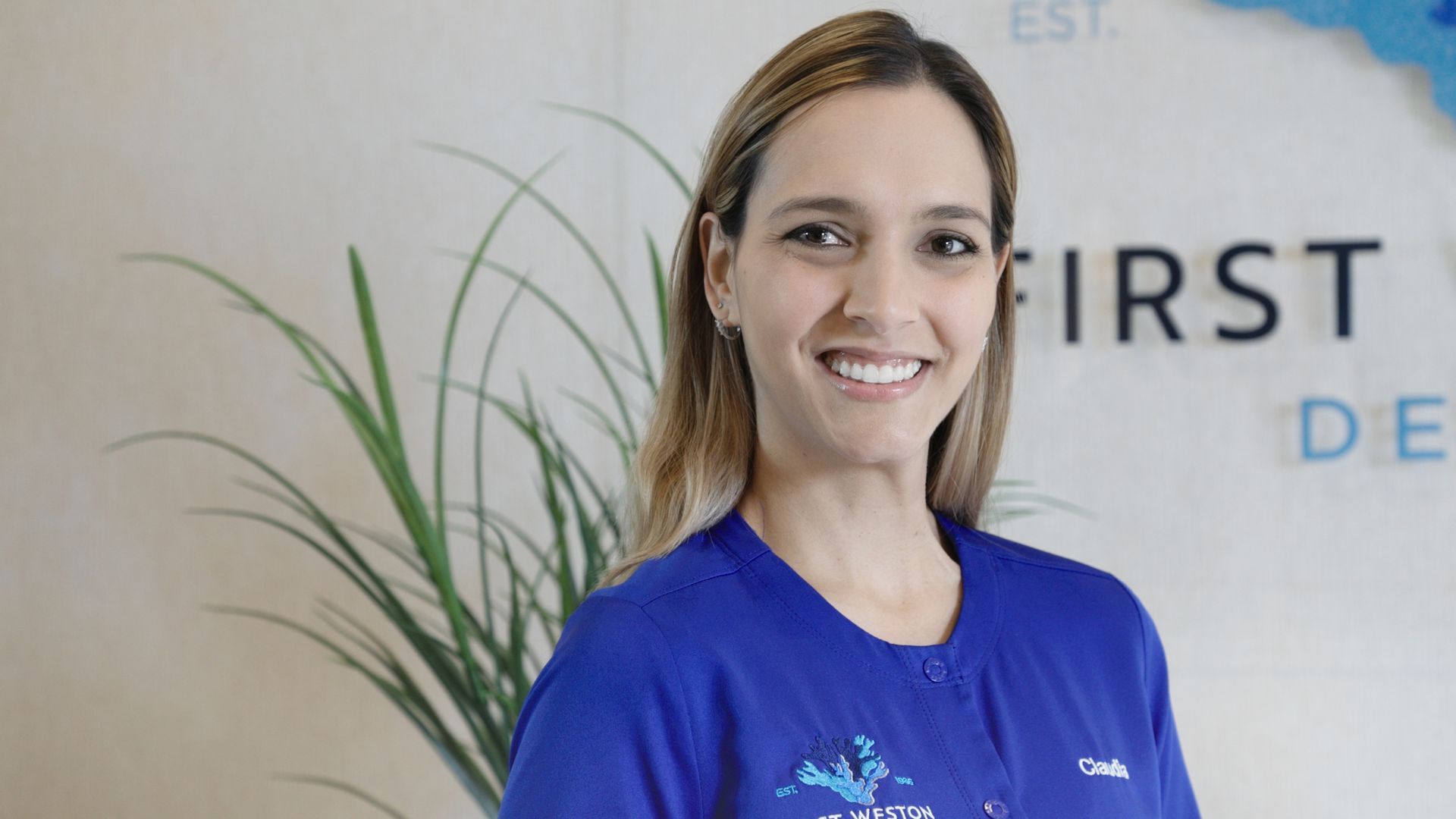A woman in a blue shirt is smiling in front of a sign that says first dental.