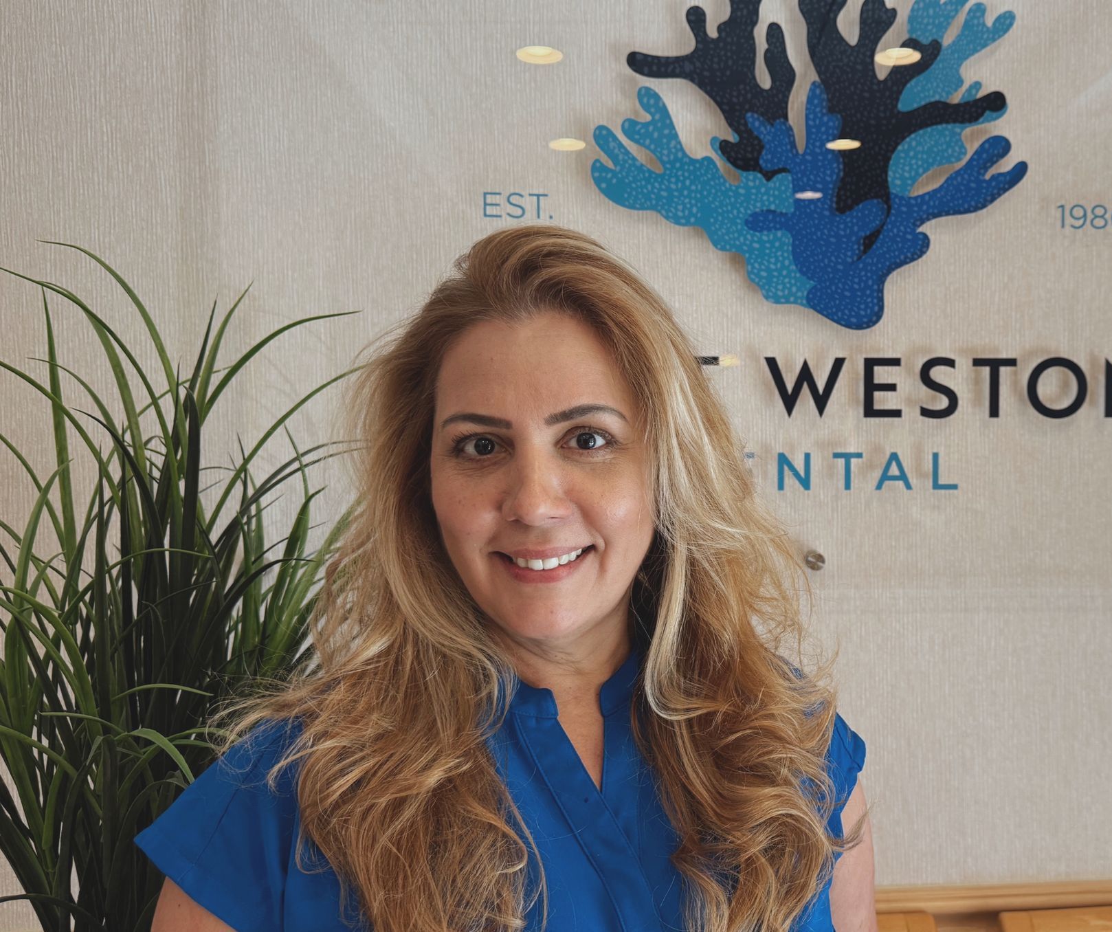 A woman in a blue shirt is smiling in front of a sign that says first.