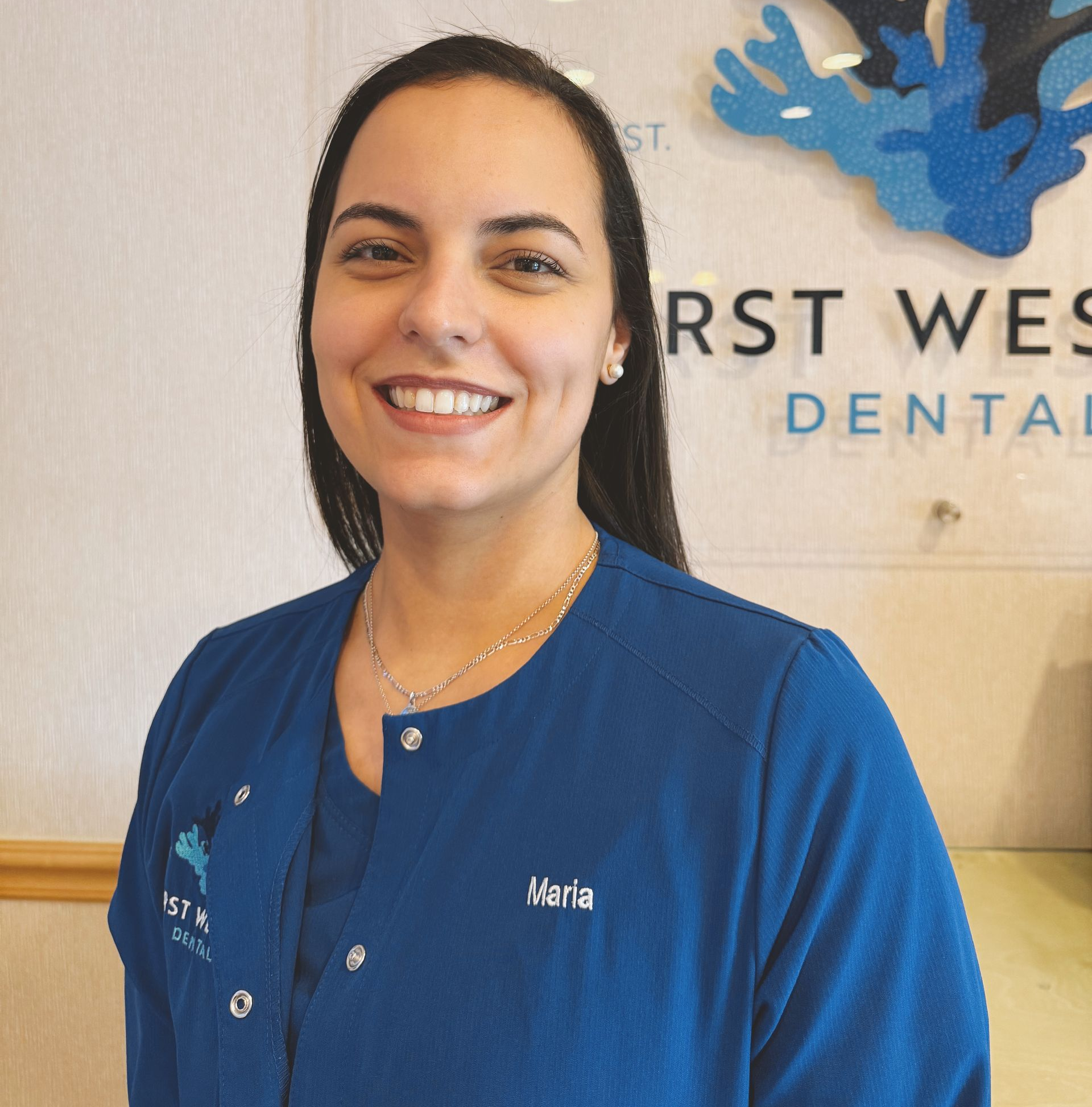 Woman in blue scrubs smiles in a dental office setting; 