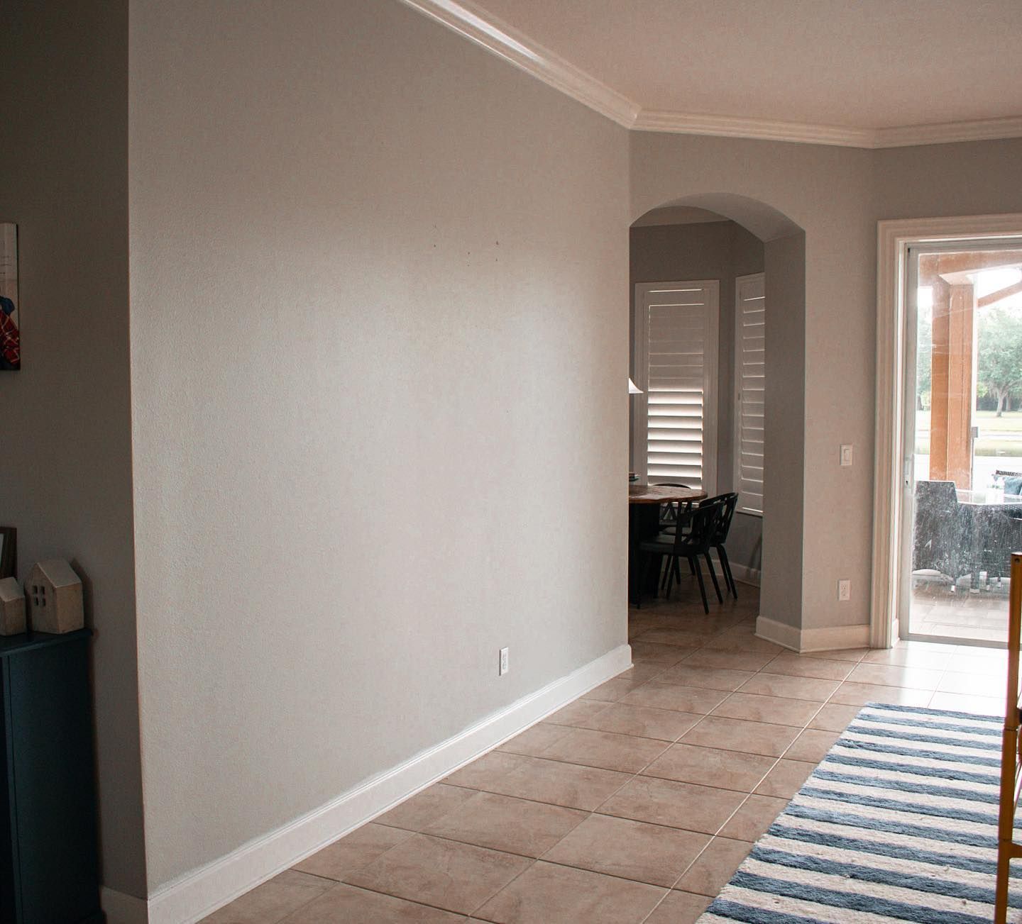 Empty beige hallway with tiled floor, arched doorway, and sunlight from a glass door.