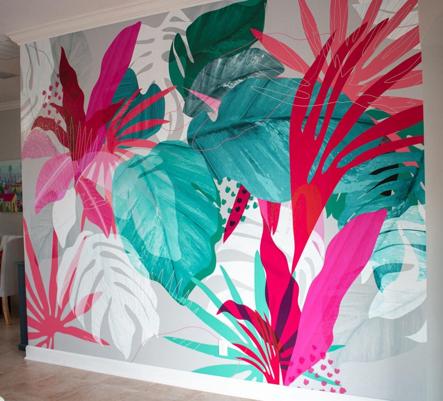 Bold tropical leaf mural in pink, teal, and white covering an interior wall