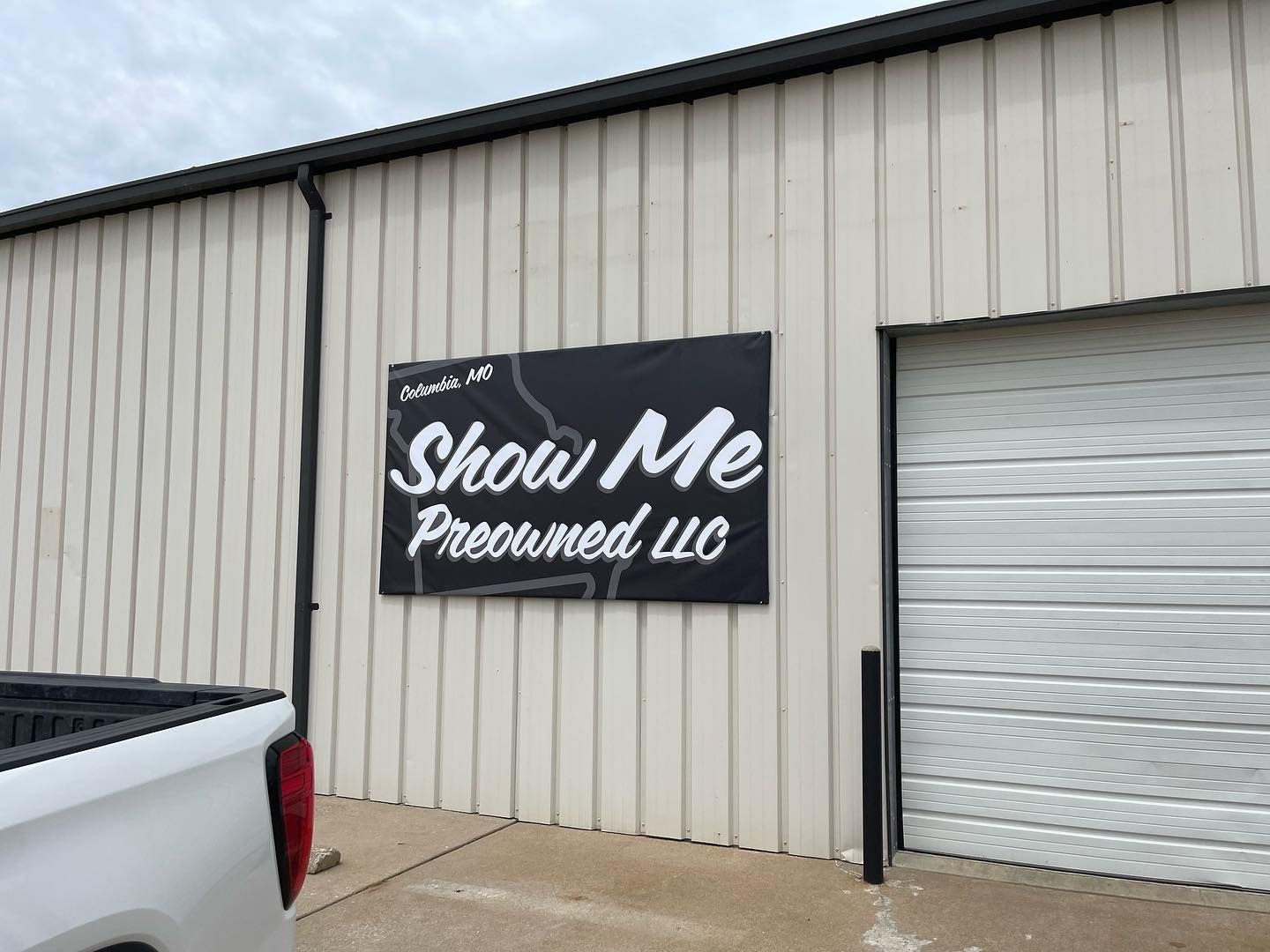 Show Me Promoted LLC sign on beige metal building beside a white roll-up door.