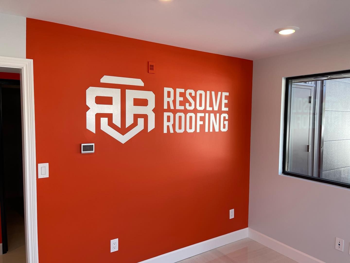 Empty red office wall with Resolve Roofing logo, white trim, and a window on the right