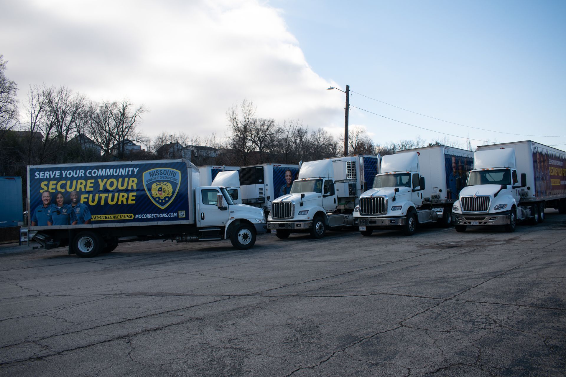 Line of white trucks and vans parked beside a blue truck with “Secure Your Future” branding in a lot