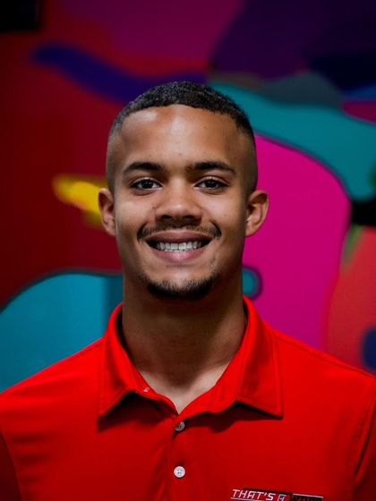 Smiling person in a red polo shirt against a colorful abstract background