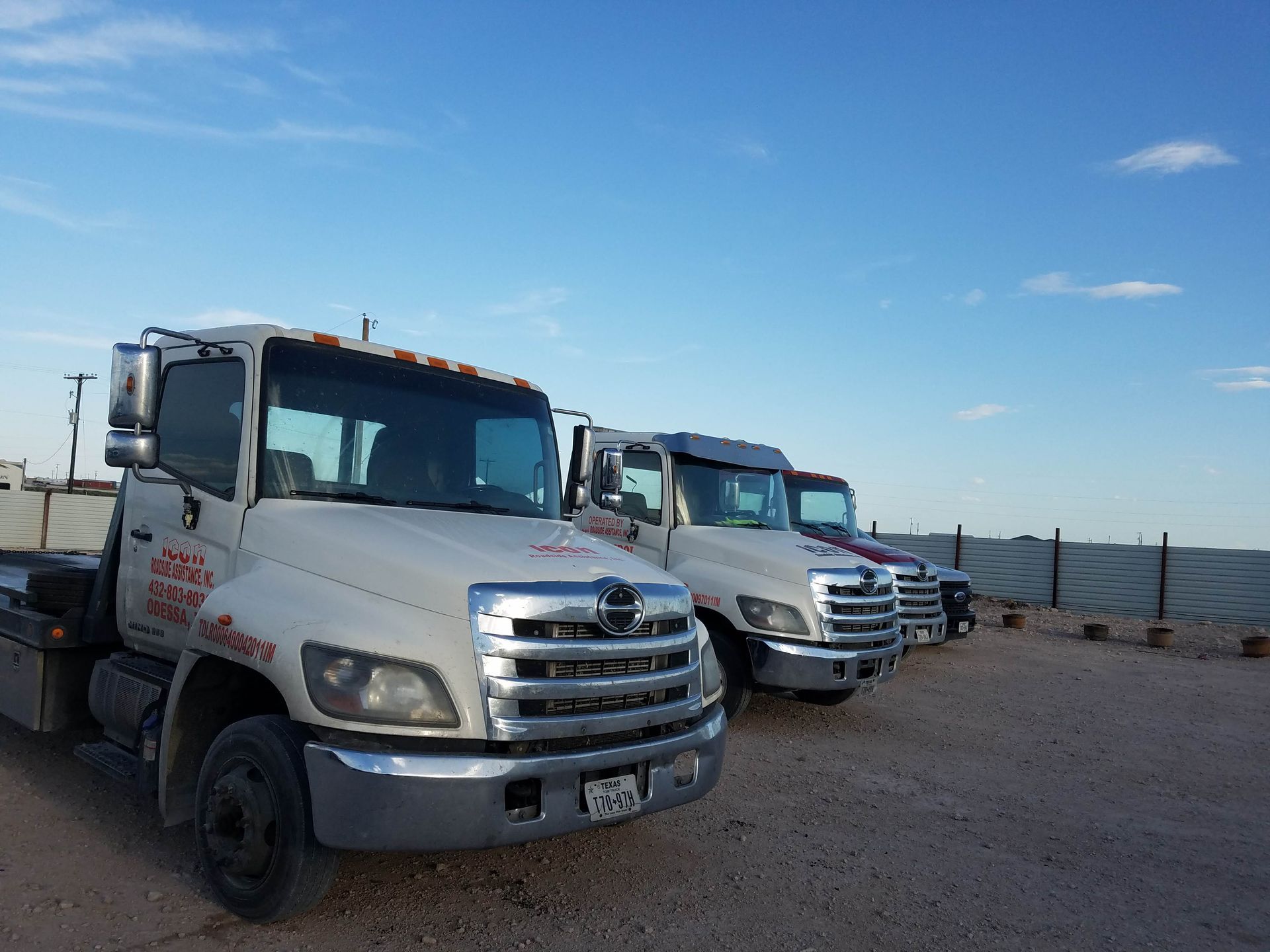 Two white tow trucks parked on a gravel lot under a blue sky