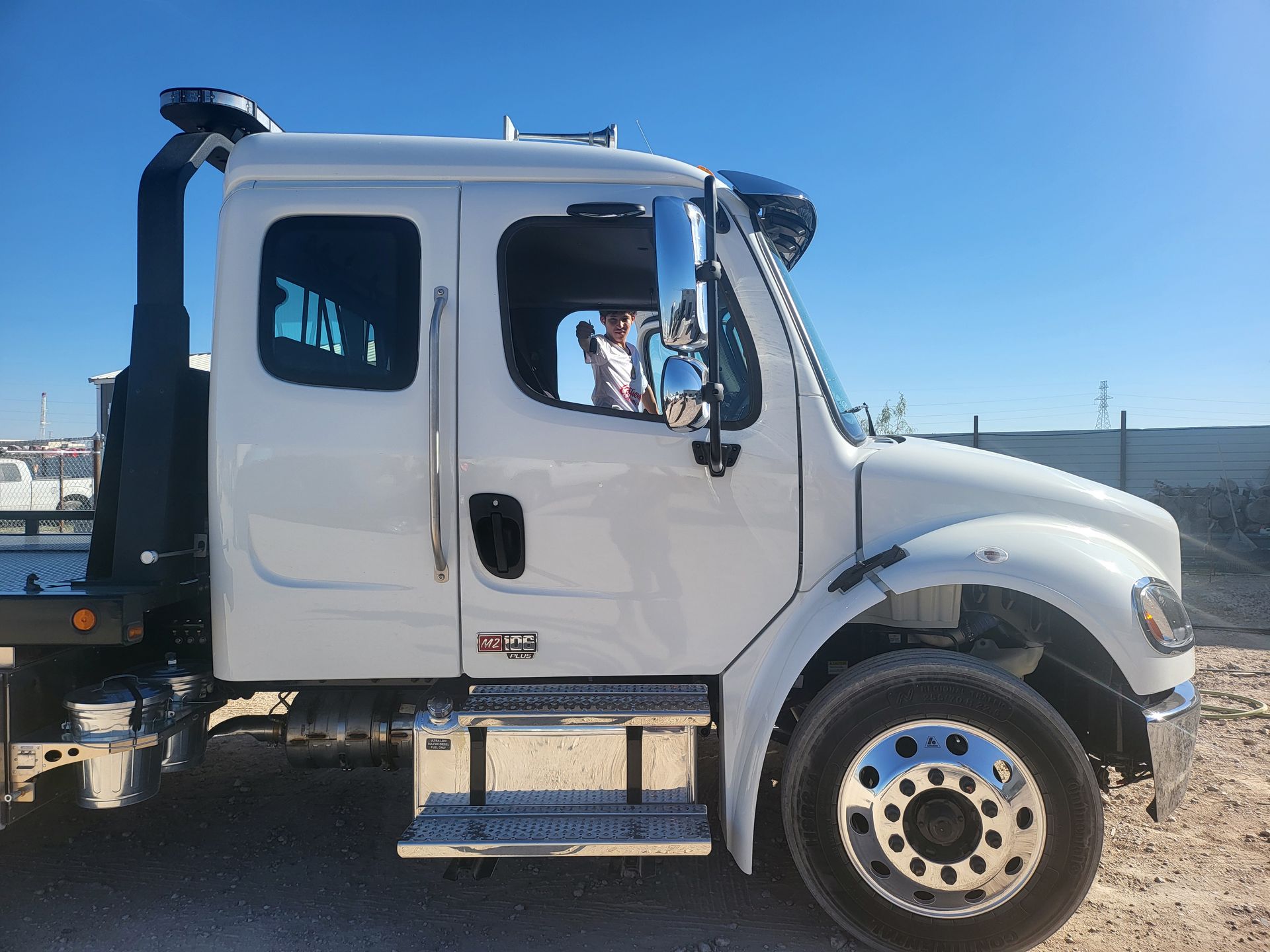 White semi-truck cab parked outdoors under a clear blue sky, side view